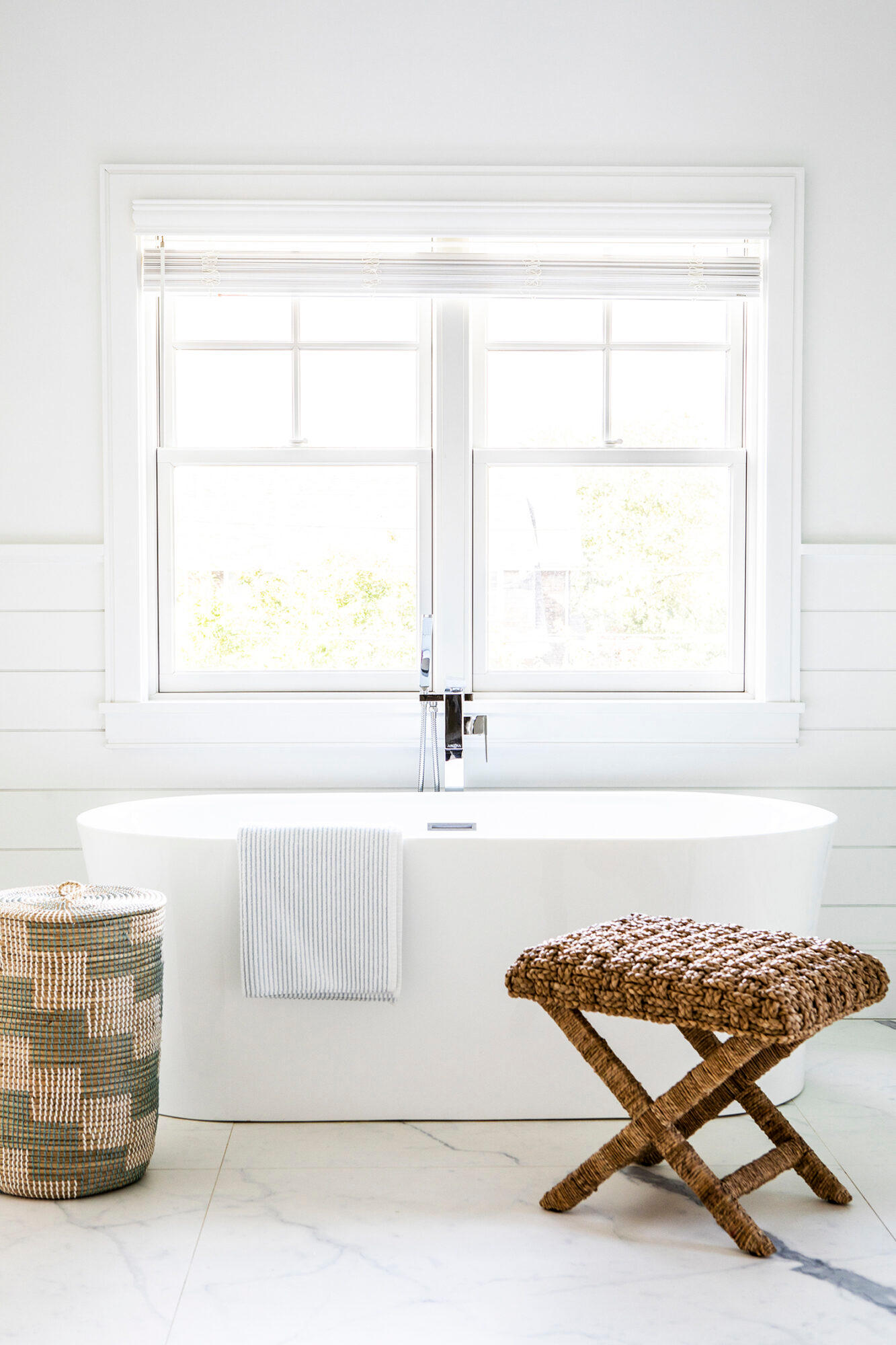 freestanding white tub in front of window and surrounded by serena and side table