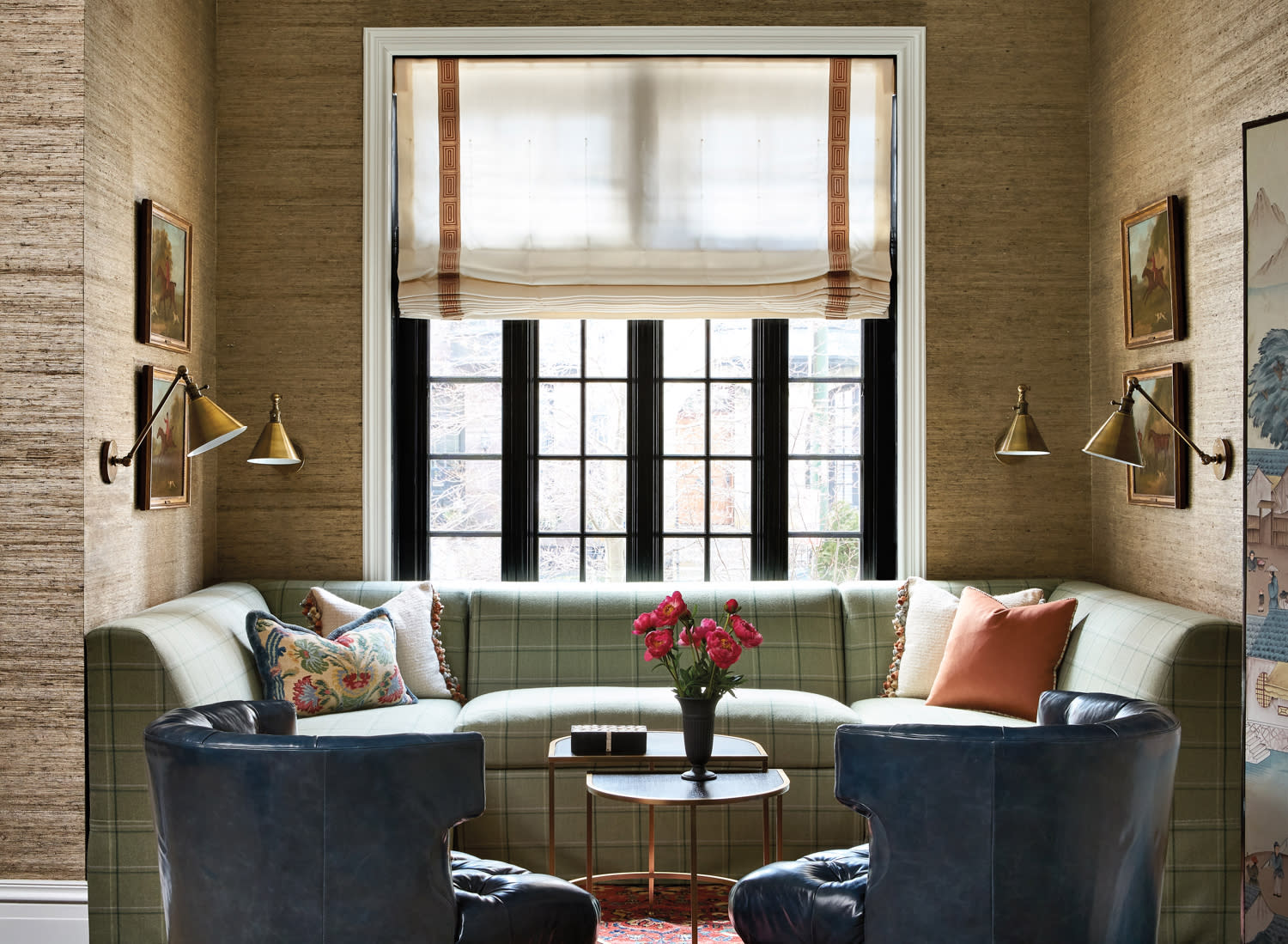 green plaid built-in banquette in front of window, two blue leather armchairs and grass cloth wallpaper