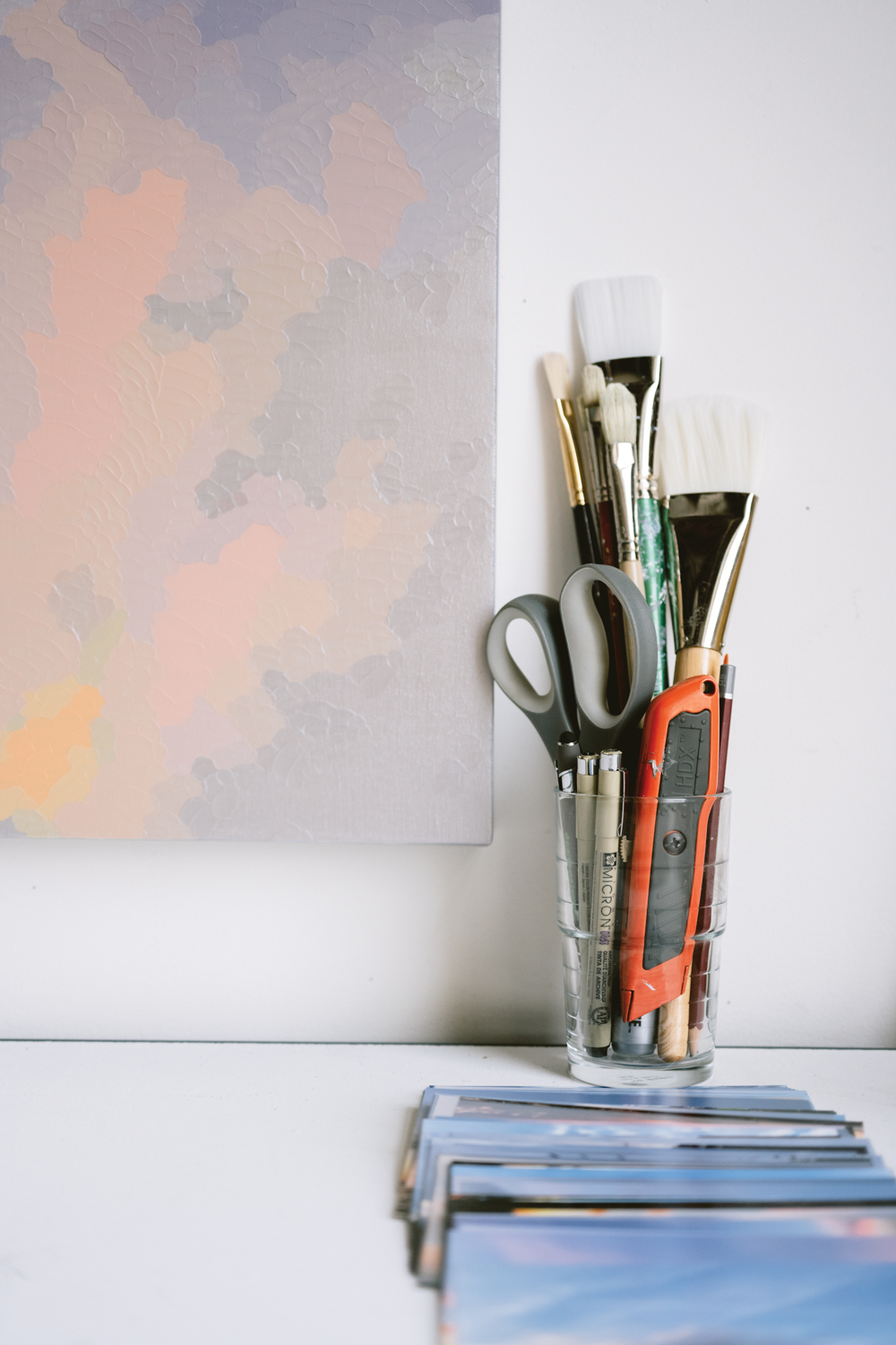 clear glass filled with tools like scissors and paintbrushes, next to painting
