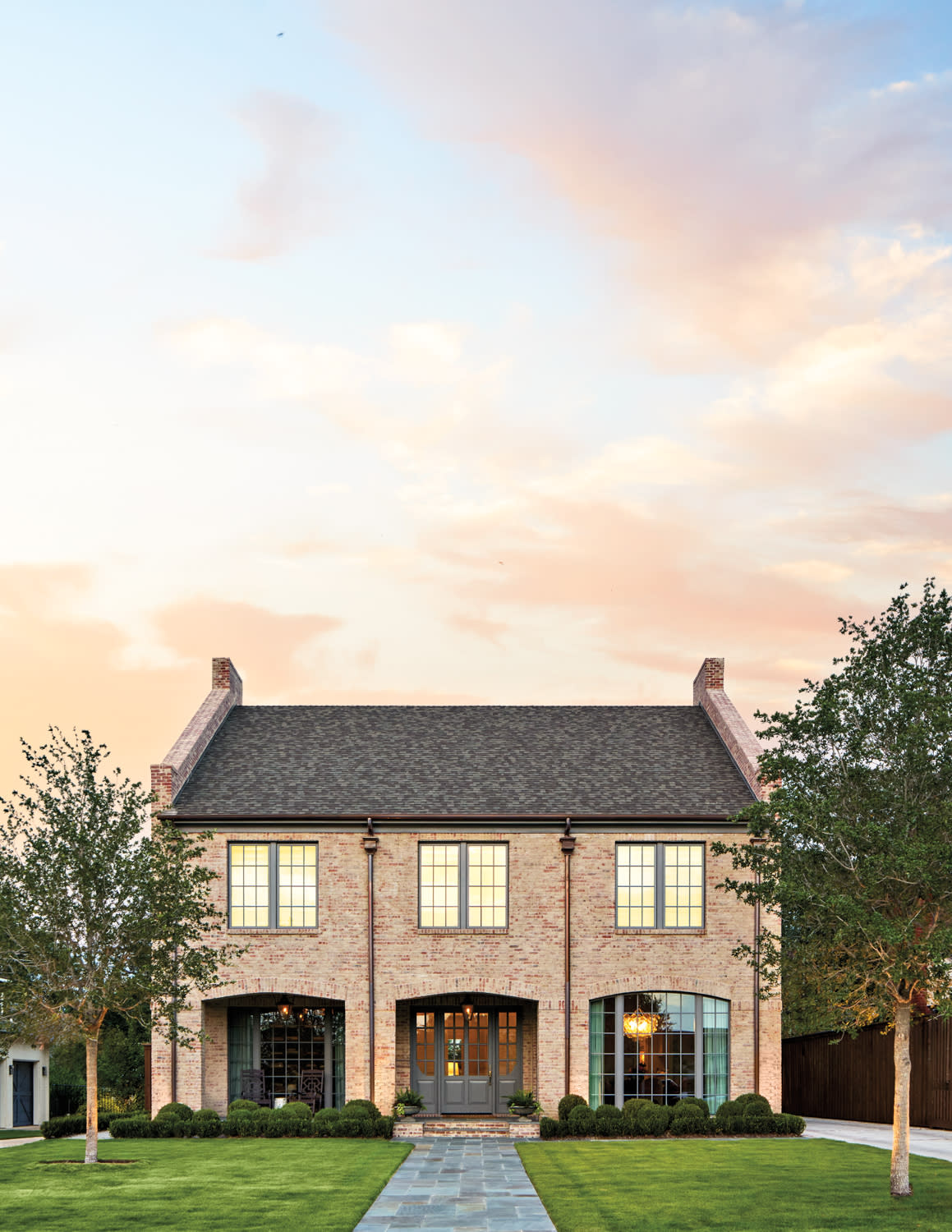 Charming two-story brick house with arched windows and a manicured lawn, set against a serene sunset sky, evokes a warm and inviting atmosphere.