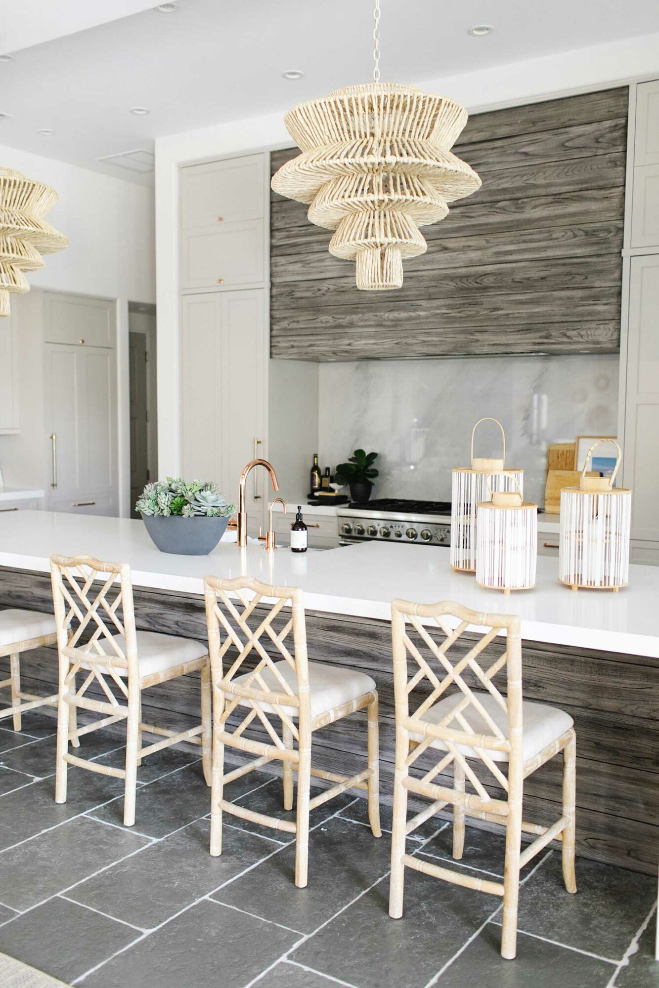 kitchen with gray wood island, dark gray flooring, rattan pendants and wicker counter stools