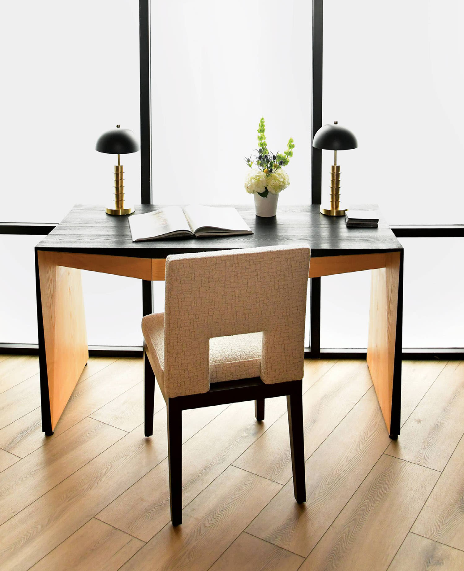 A wooden desk with two lamps and a chair positioned near windows.