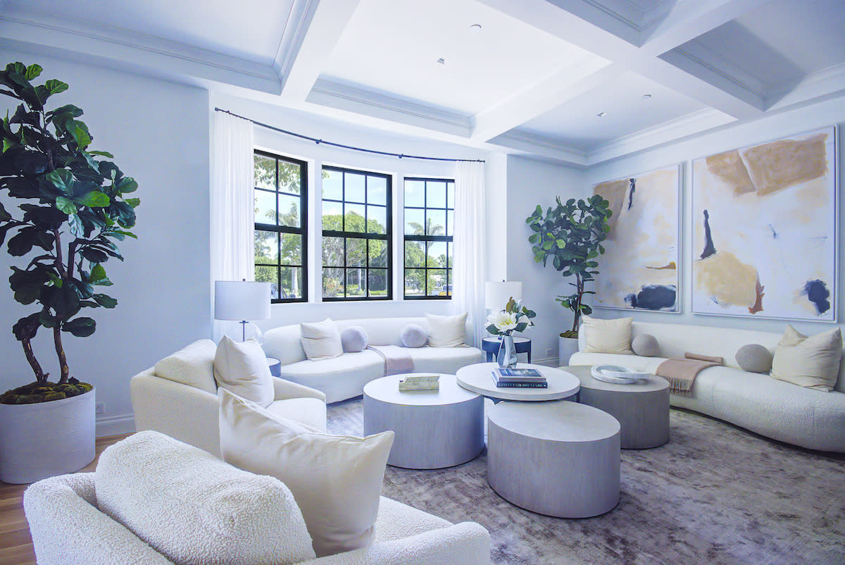 A living room with white furniture and a large painting hanging on the wall.