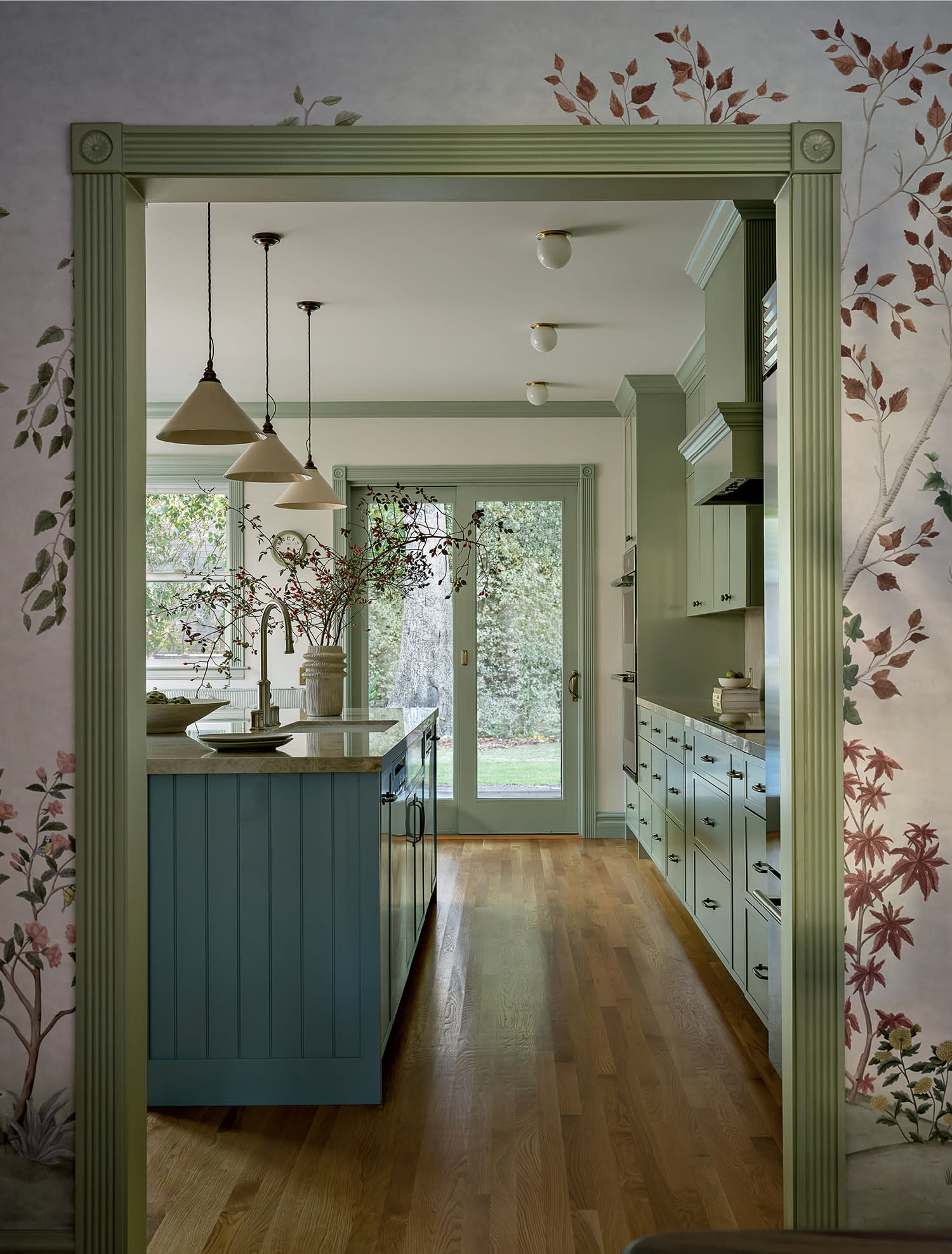 traditional kitchen seen through a doorway flanked by green trim and a vine-like wallpaper