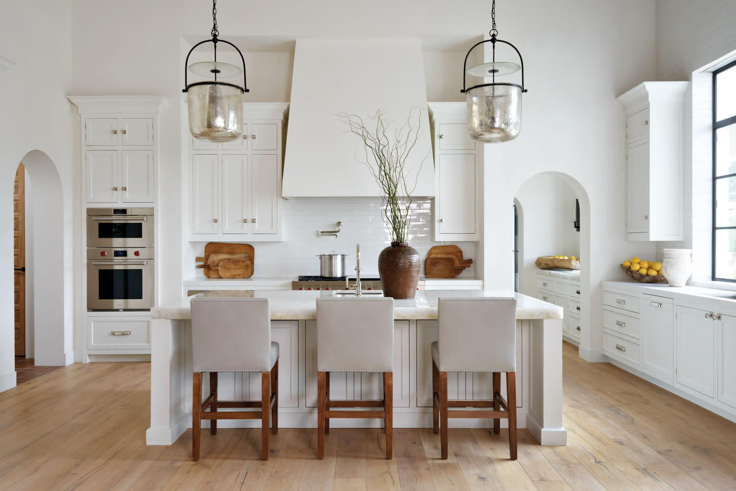 white kitchen with gray stools that pull up to white quartz-topped island and smoked glass pendant lighting