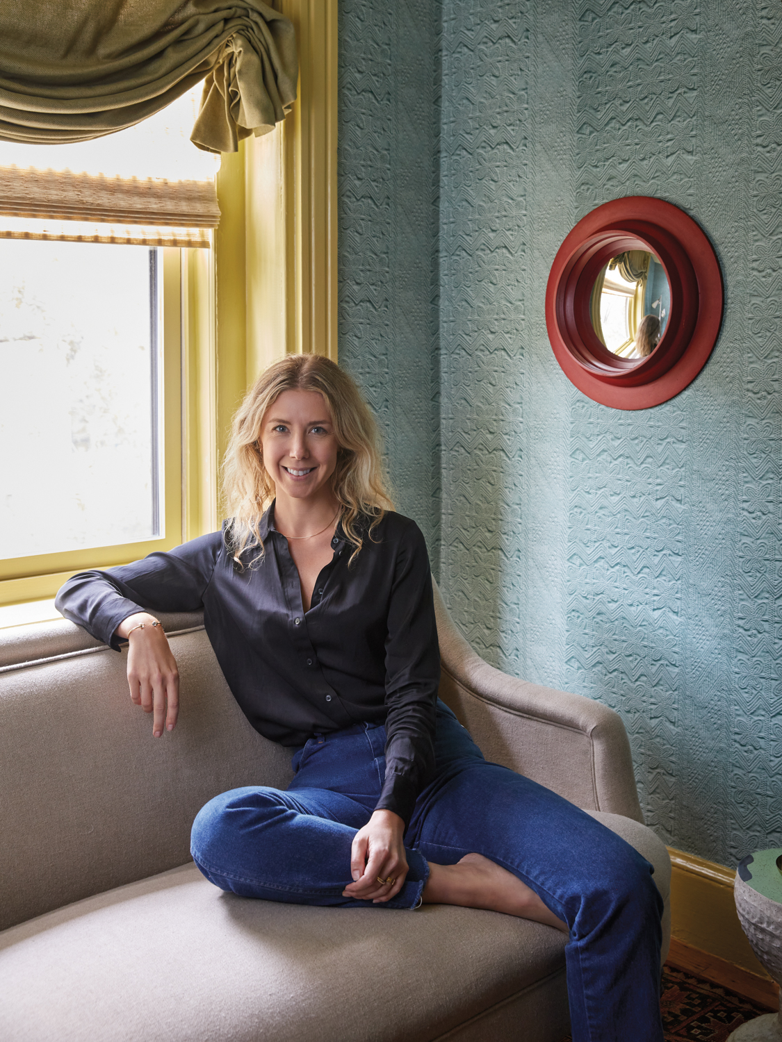 Jessica Stambaugh sitting on a couch in a blue button-down shirt and jeans.