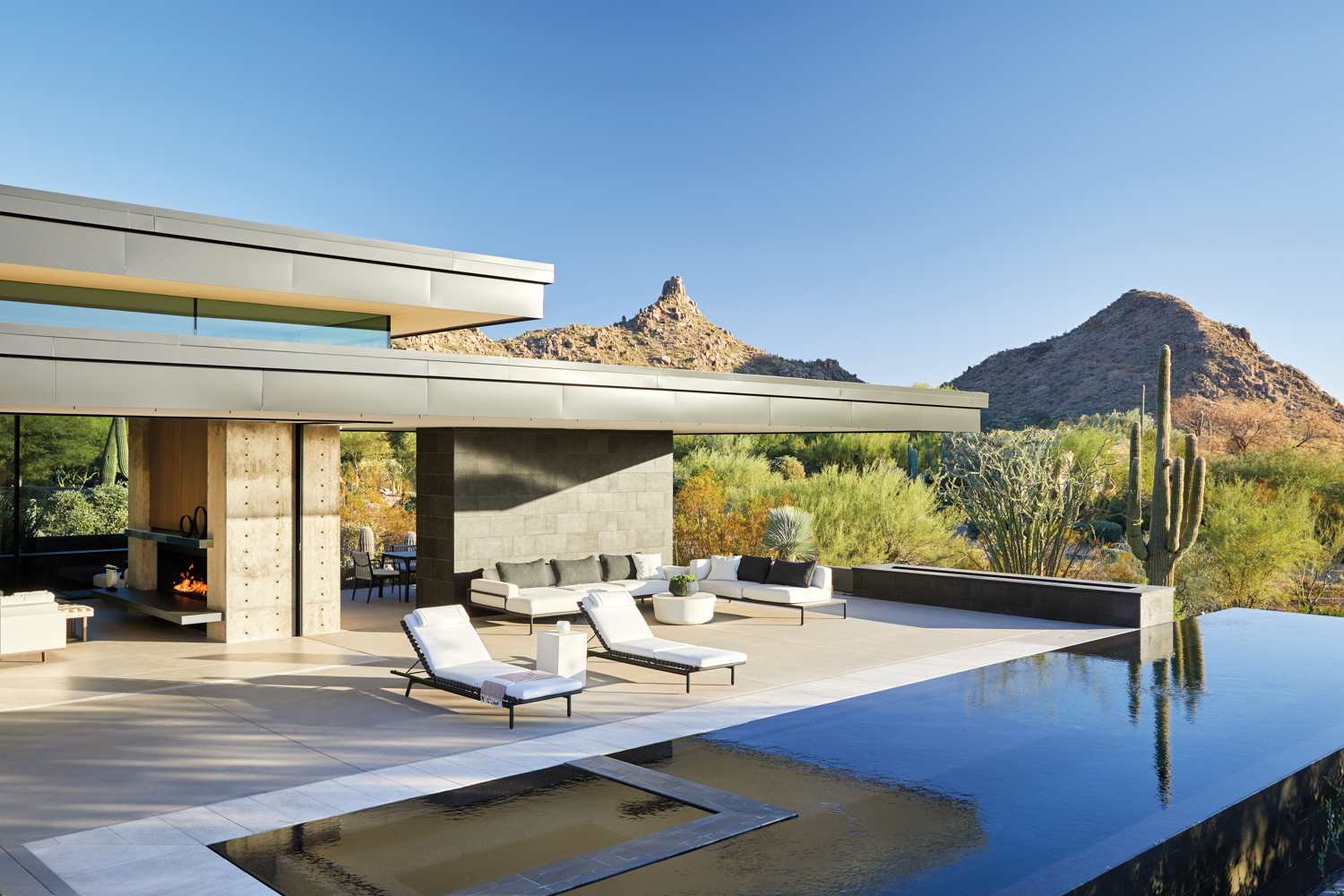 a patio with multiple seating and dining areas borders an infinity pool with mountain views