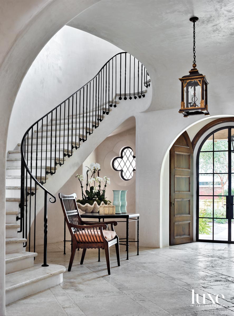 Entryway with plaster walls, curving staircase and quatrefoil-shaped window