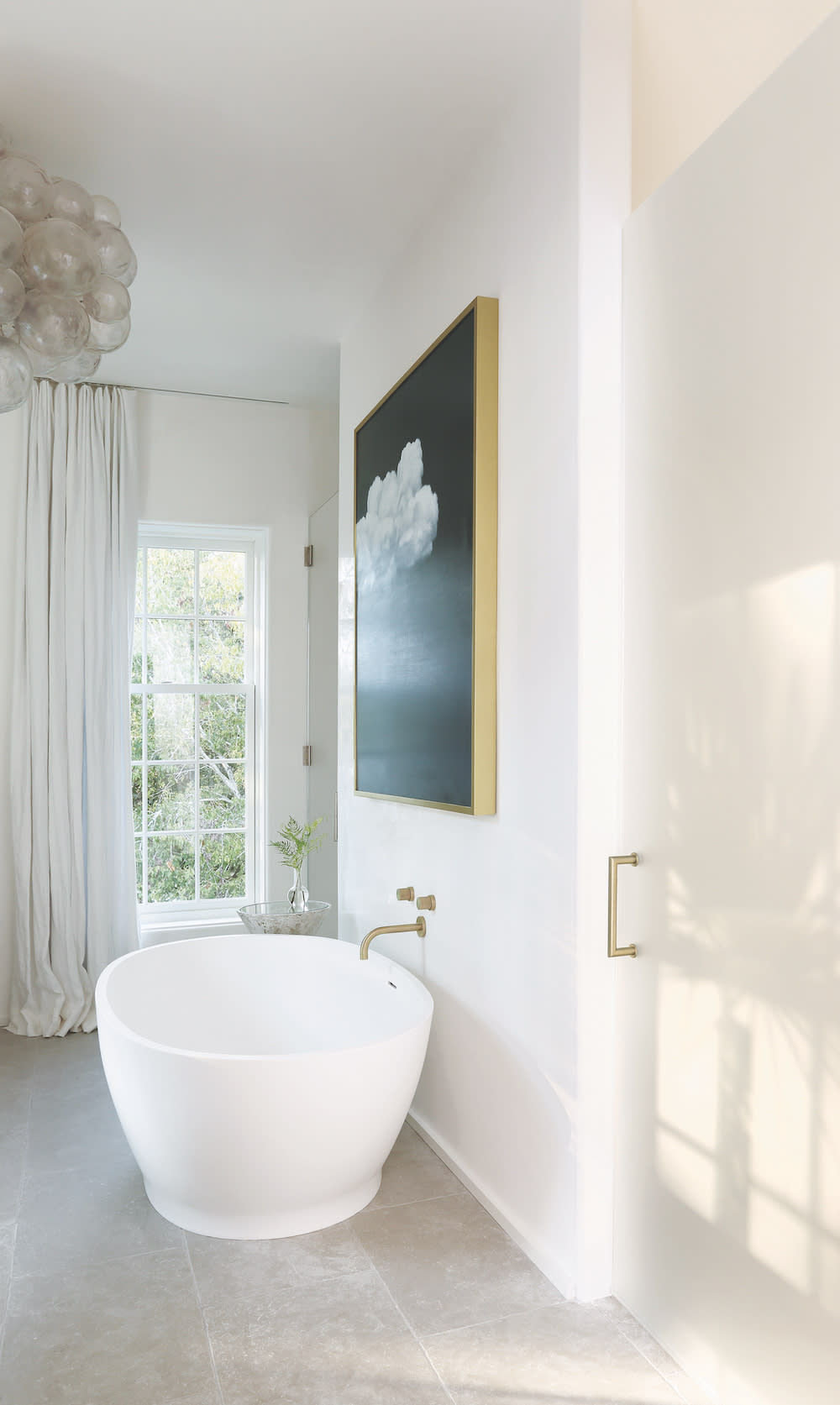 Paris Grey Limestone by Francois & Co in all white bathroom with white stand alone tub, gold fixtures, bubble lighting and bold artwork