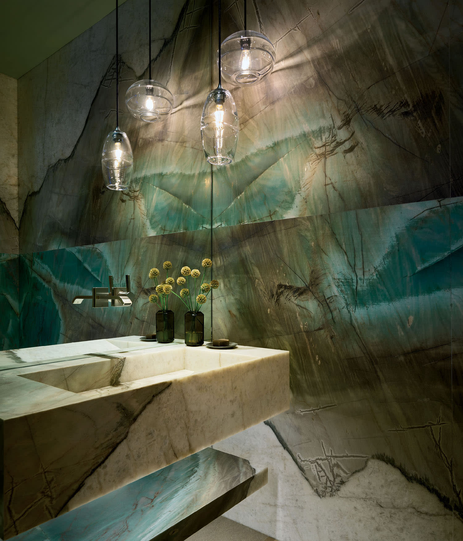 A vanity in a bathroom with blue-green quartzite walls and pendant lamps.