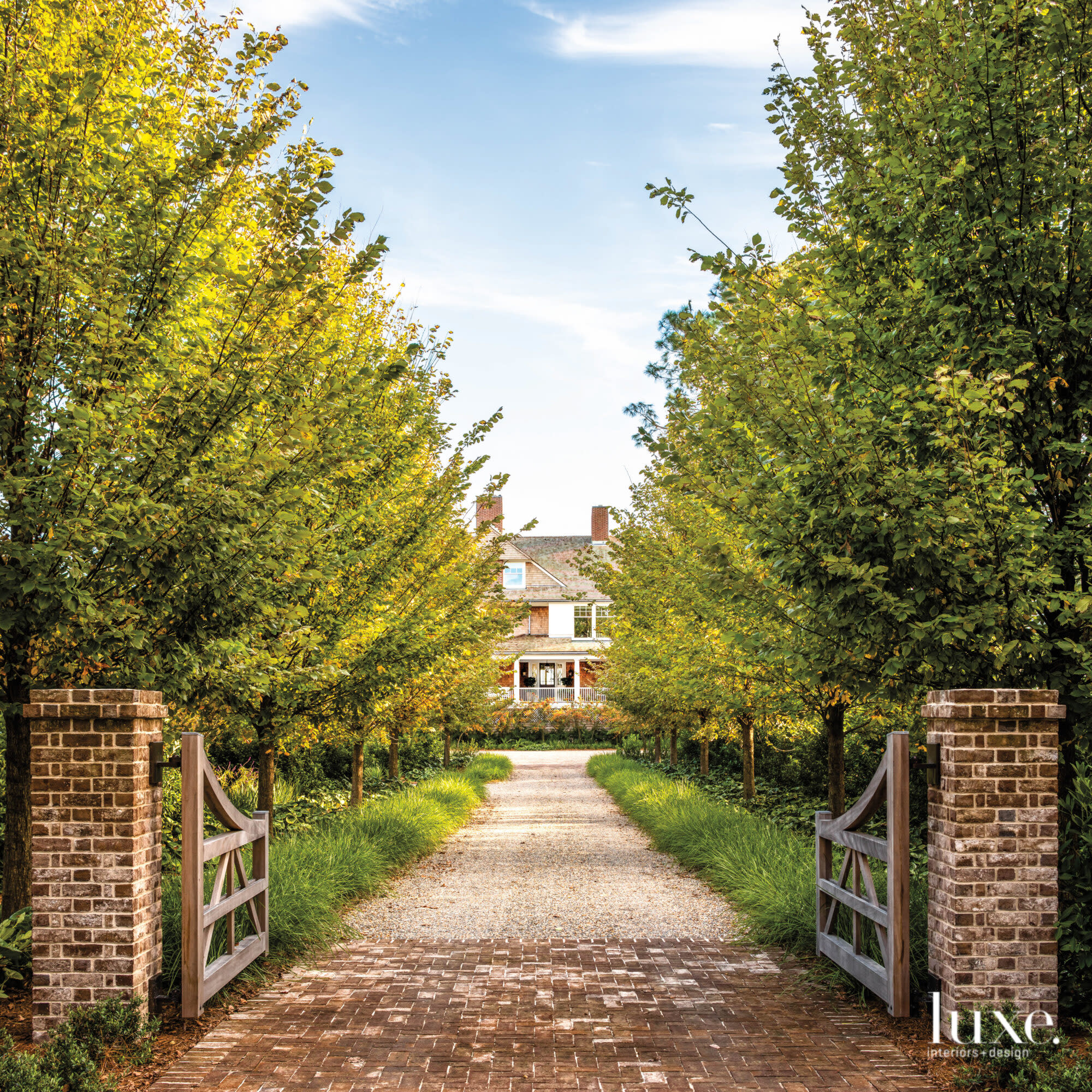 Open gate and view of long driveway to a residence framed by tall trees
