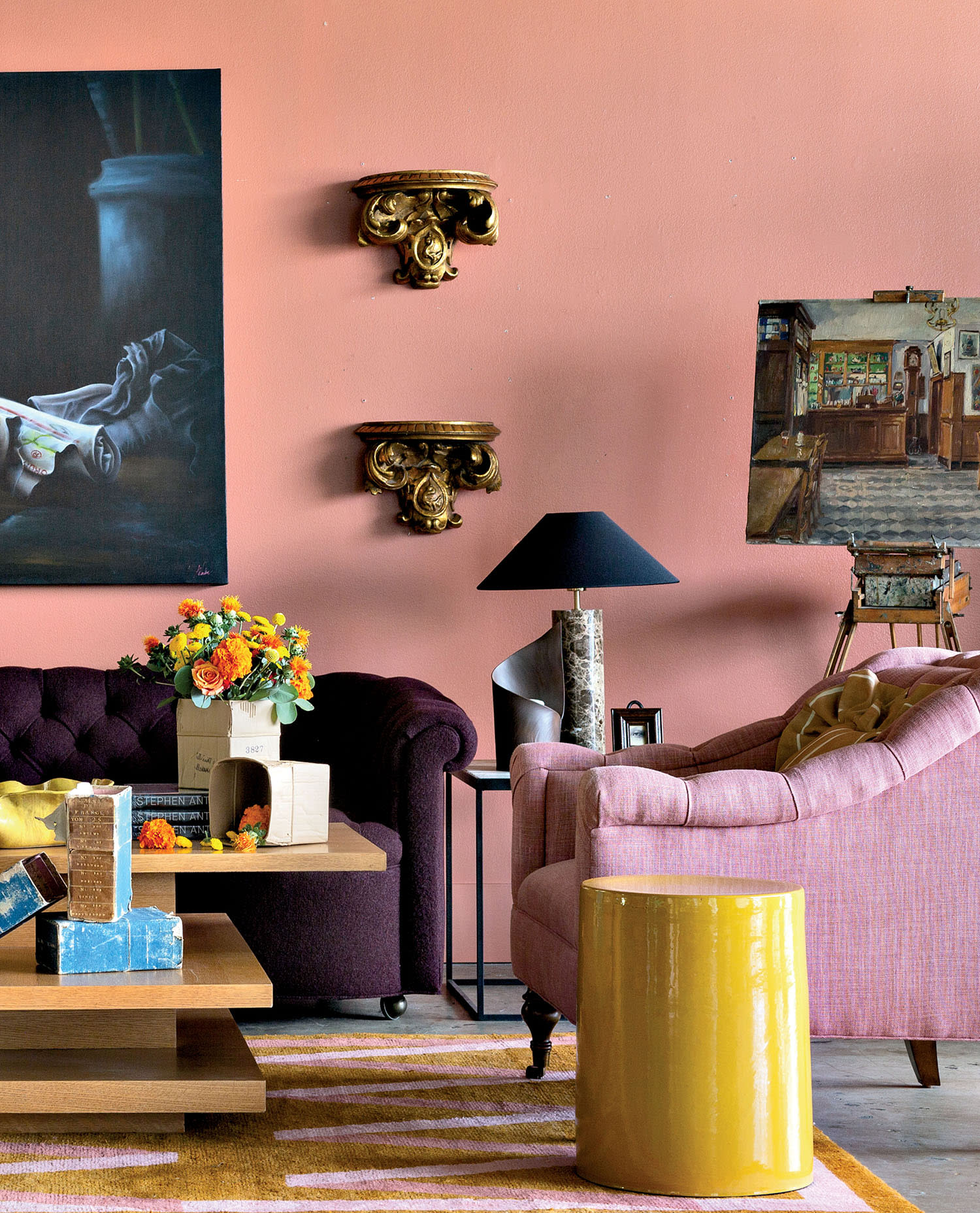 A pink armchair and purple sofa sit in a room with bright flowers and a yellow accent table.