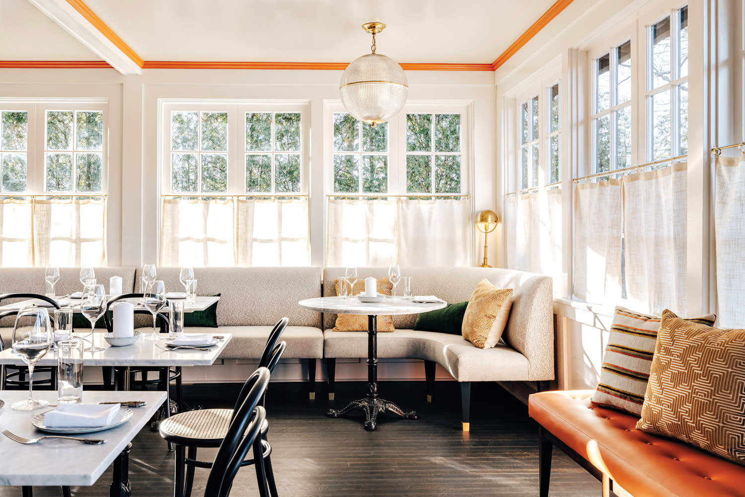 mid-century France aesthetic restaurant with window-clad dining room and orange accents