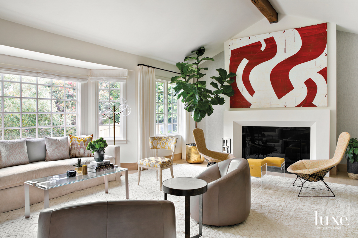 White painted living room with bold artwork over the fireplace and multiple seating areas.