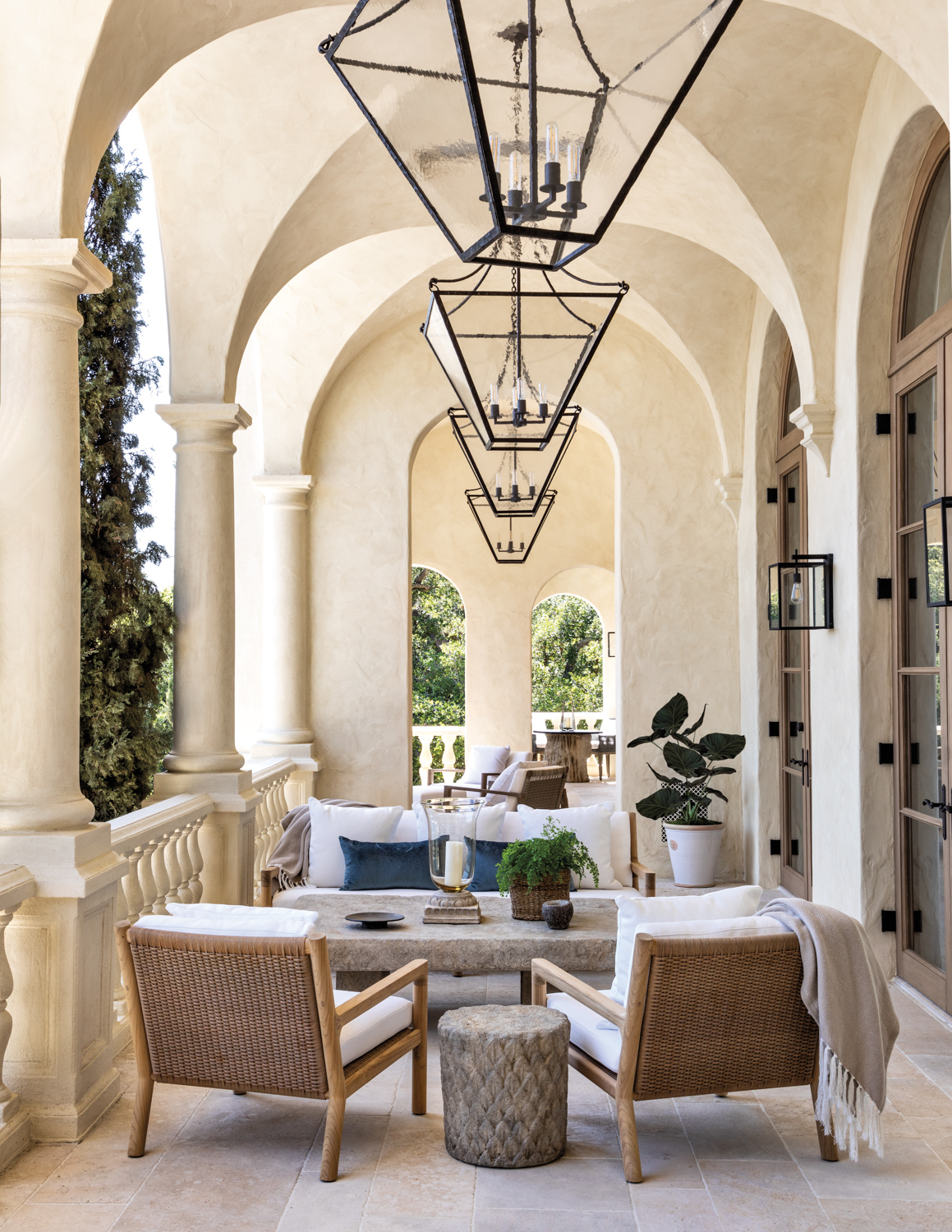 Outdoor veranda with a concrete coffee table, light colored outdoor sofa and a row of lanterns hanging above