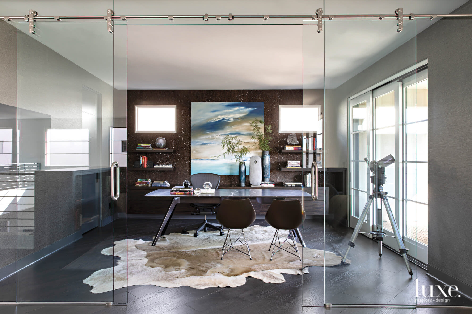 The study has a hide rug, black cork wallcovering and a blue-and-white-and-tan painting behind the desk.