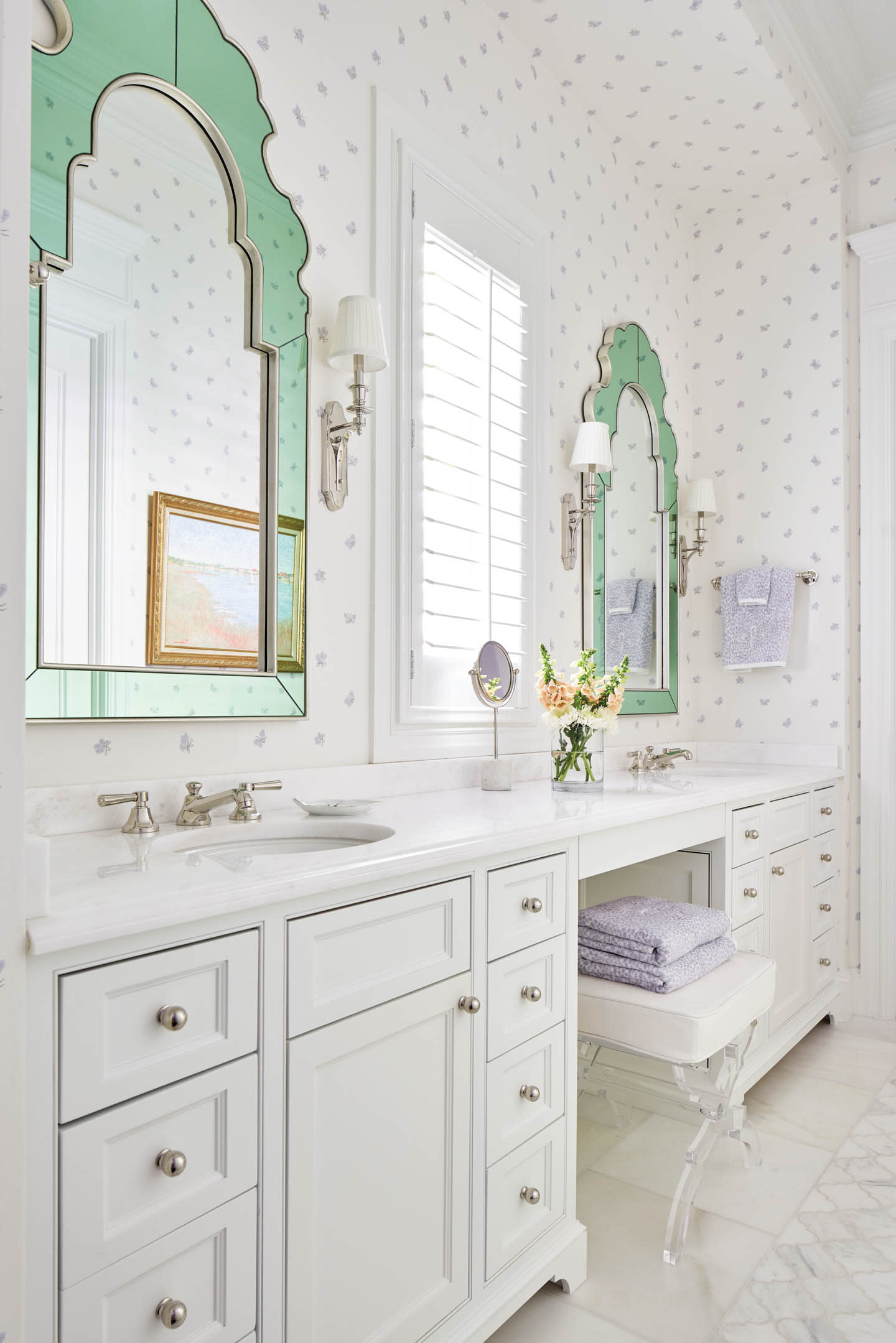 Bright and whimsical bathroom with white cabinetry, pastel polka dot wallpaper, and twin mirrors framed in ornate mint green.