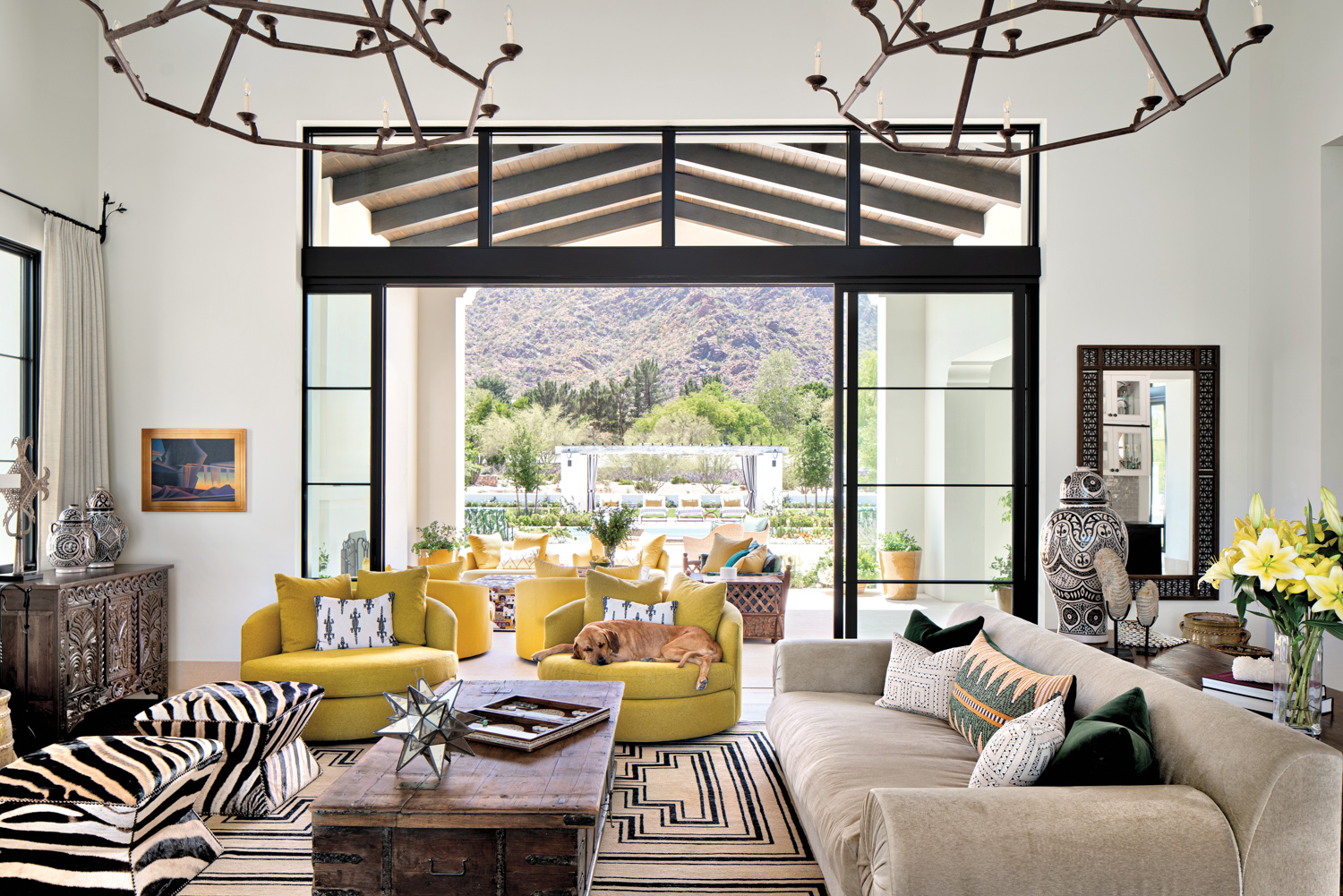 Living room with two yellow swivel chairs, a taupe couch, zebra stools and glass doors opening to a patio