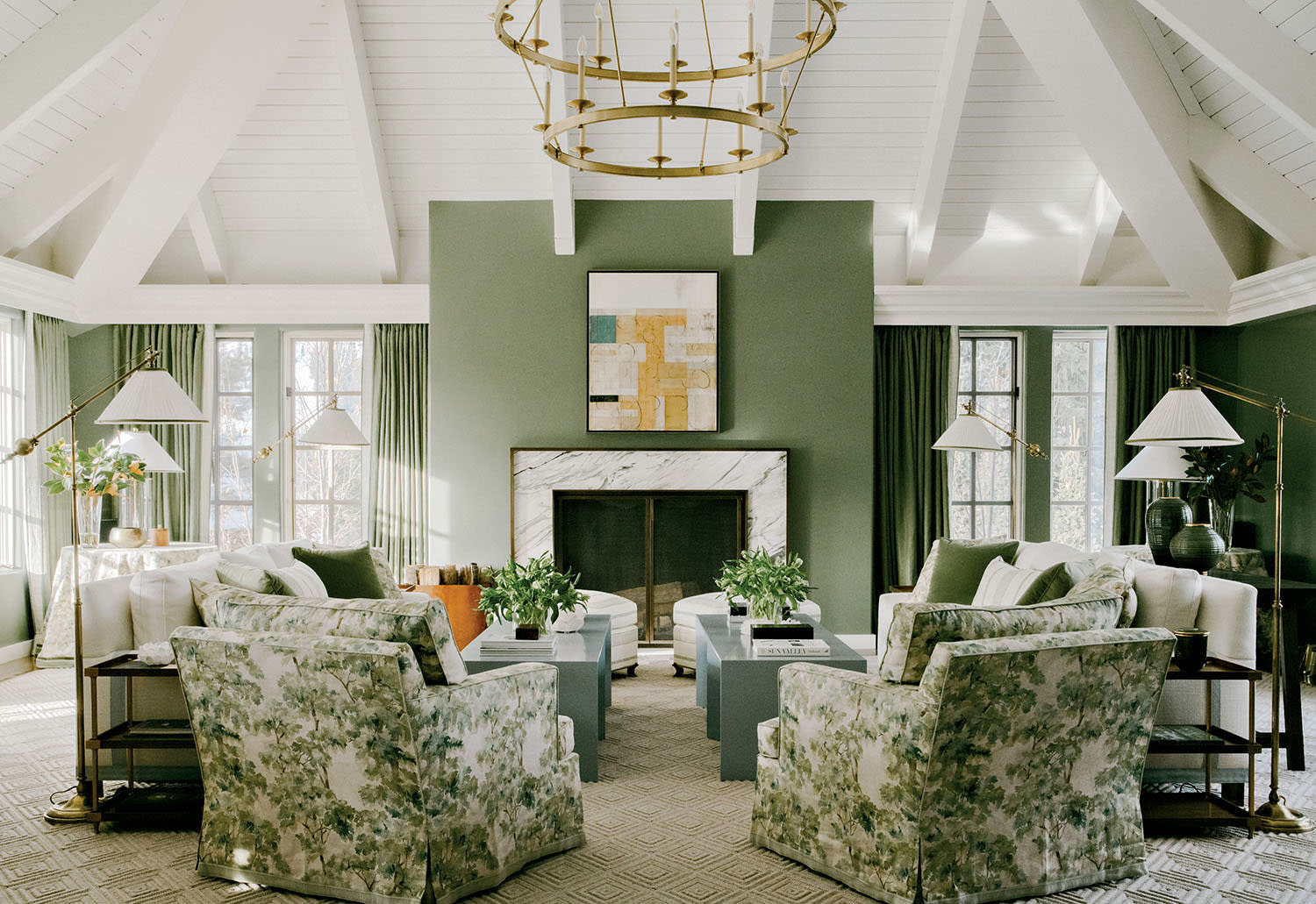 A living room with green walls, patterned armchairs and gray coffee tables near a fireplace.