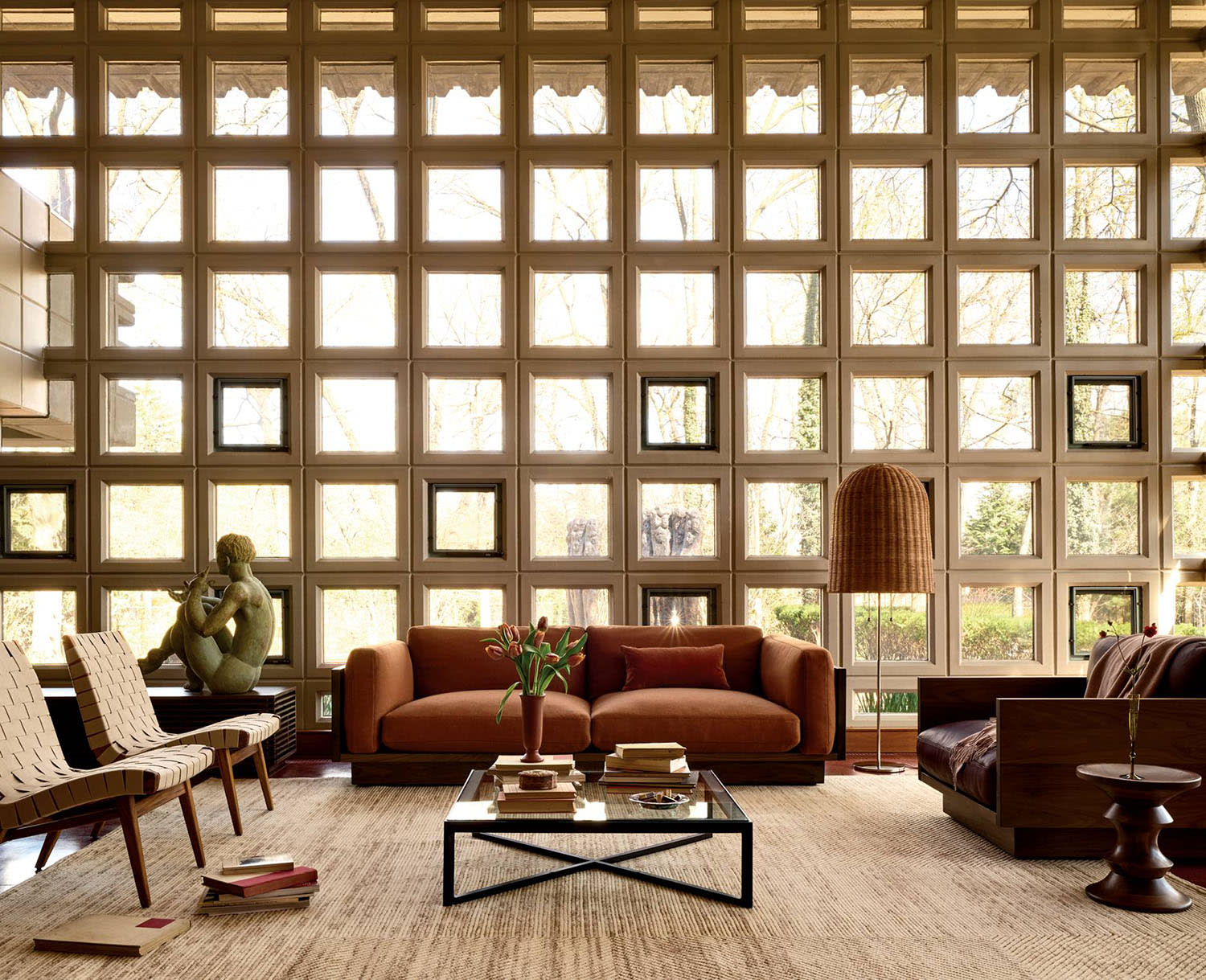 A rust-colored sofa sits on a rug alongside armchairs, a statue and a coffee table.
