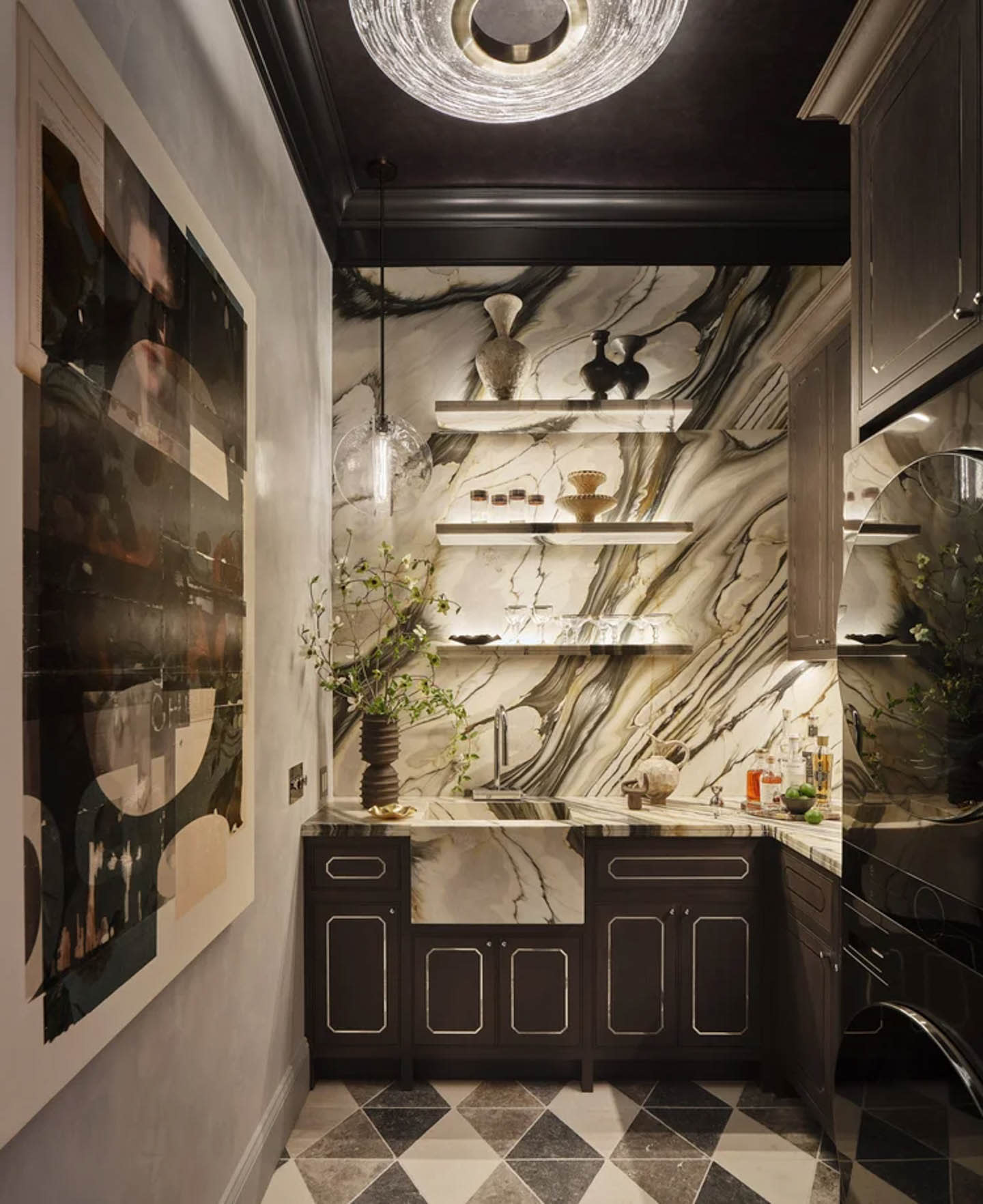 A luxurious laundry room features a marble backsplash with bold patterns, dark cabinets, and floating shelves. A round glass light hangs from a dark ceiling, illuminating plants and ceramic decor, creating an elegant, sophisticated atmosphere.