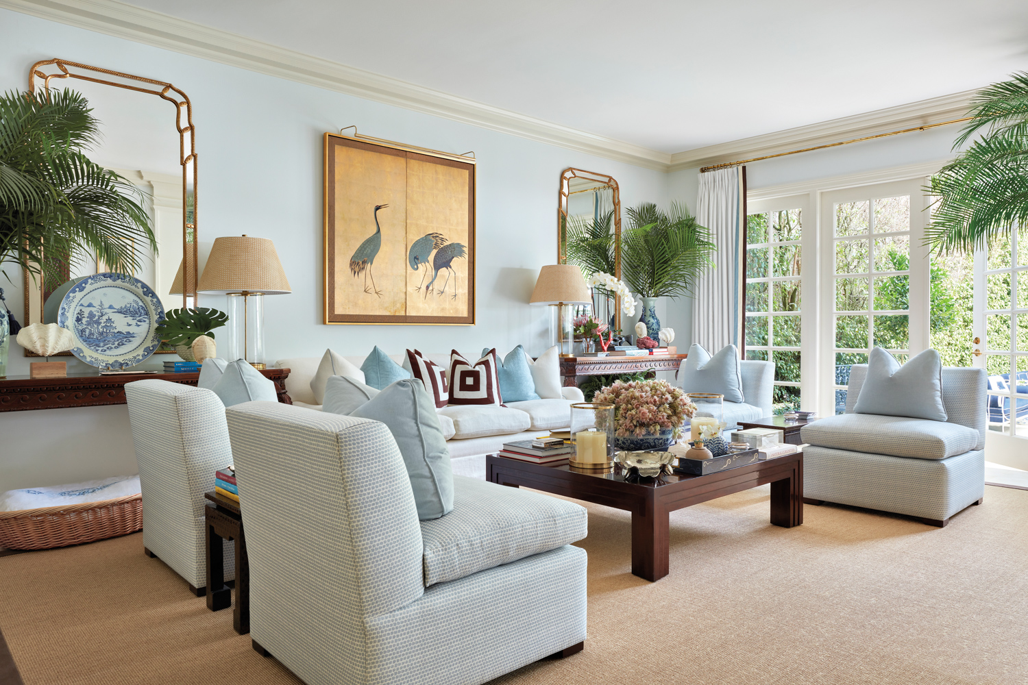 living area with light blue walls, light colored sofa and slipper chairs, gold leaf panels and square wood coffee table