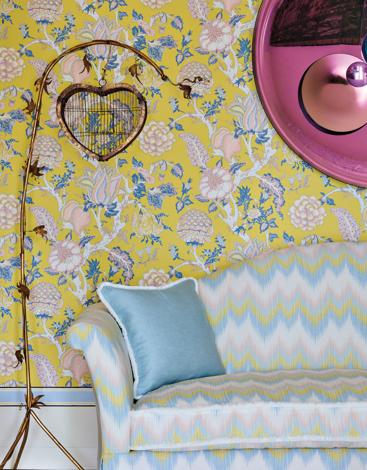 A bright yellow wallpaper with blue and pink florals is the backdrop for a sofa with the same colors