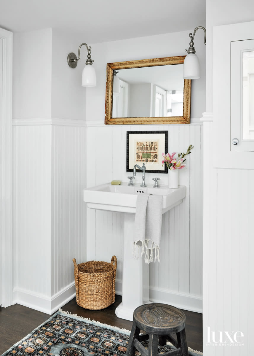 A gilt mirror hangs above a pedestal sink in a white bathroom.