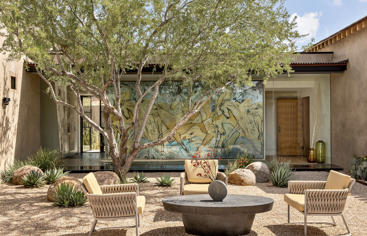 An outdoor seating area with chairs around a stone table with a tree giving shade nearby.