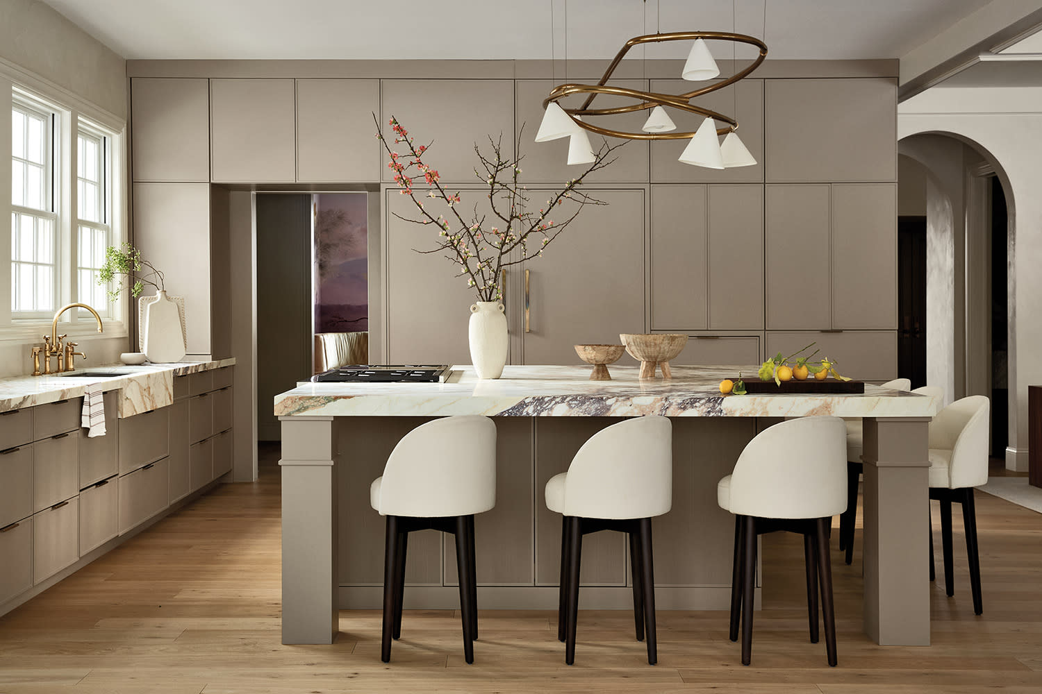Kitchen with taupe cabinetry, a marble island, modern pendant lights, and floral branches in a vase.