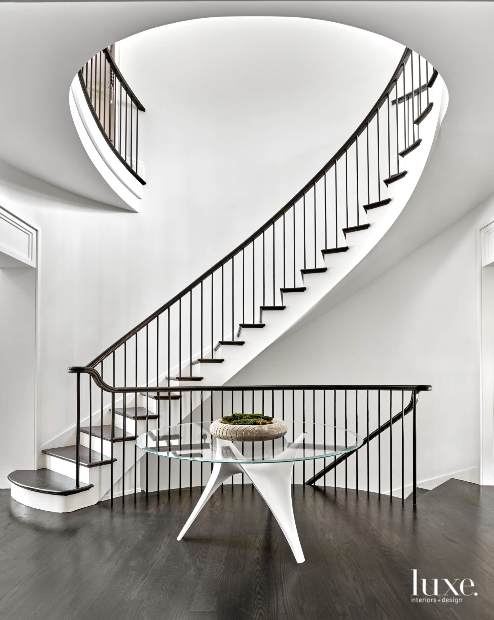 A glass-topped table sits in front of a curved grand staircase.