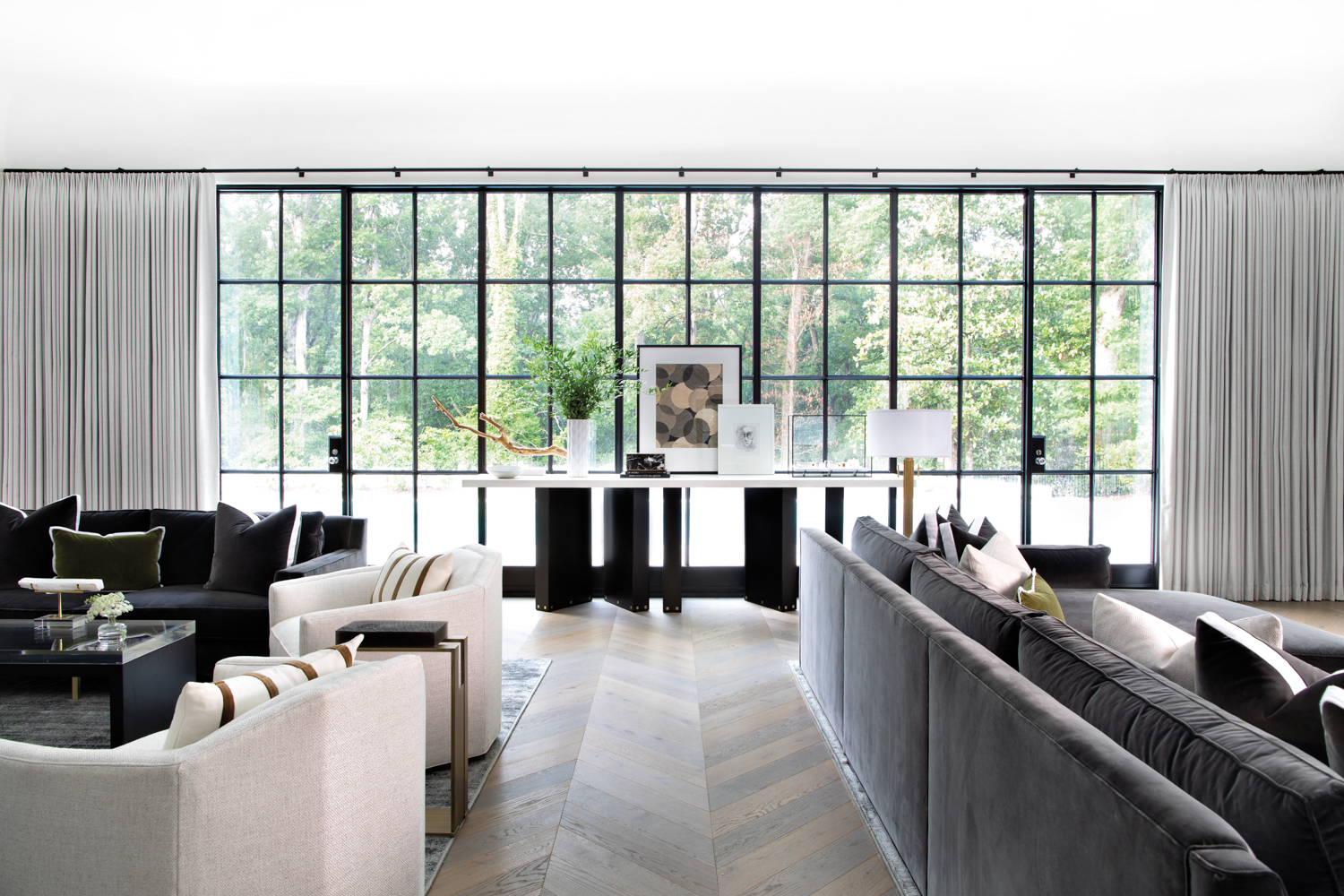 A spacious living area featuring multiple seating groups and a modern console table before a bank of metal windows