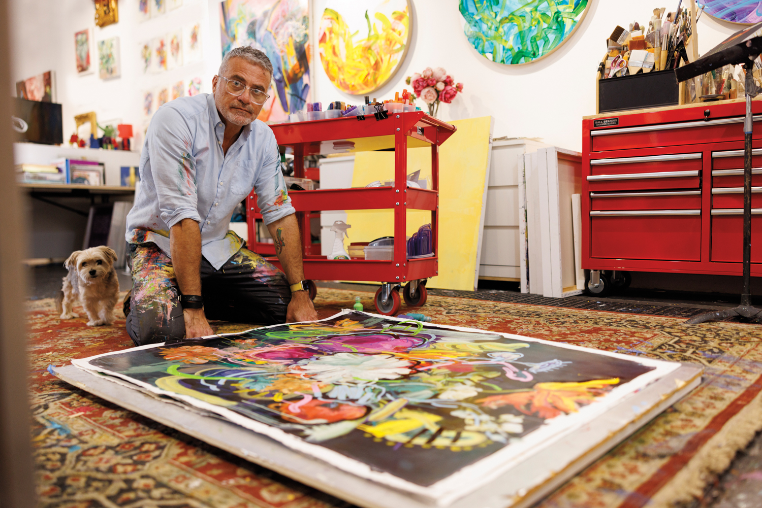 artist carmelo blandino with his morkie kneeling in front of a painting on the floor of his studio