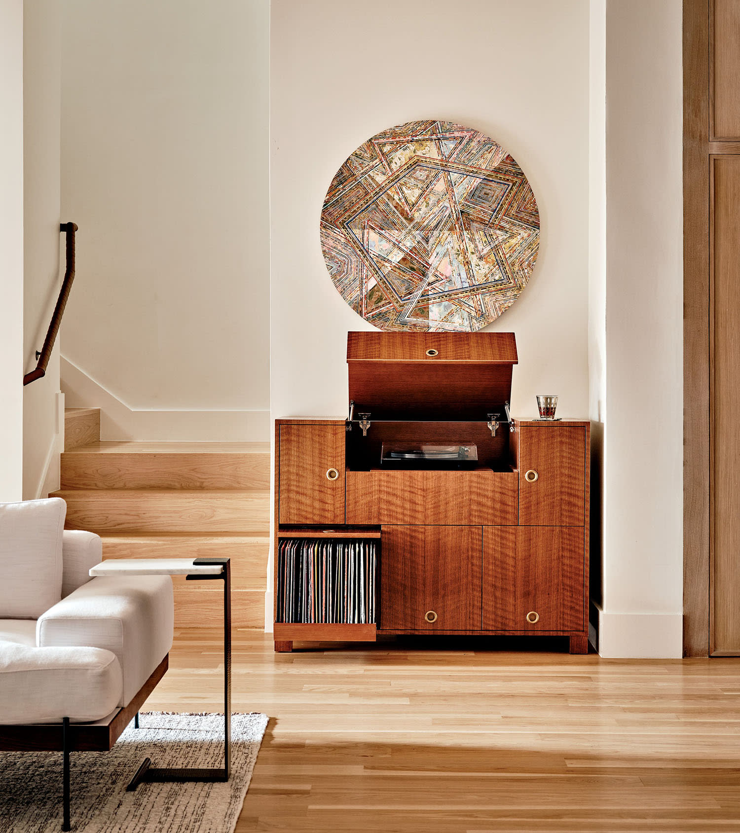 Stylish living room with a wooden cabinet holding vinyl records and a record player. Circular abstract artwork hangs above. Light, cozy ambiance.