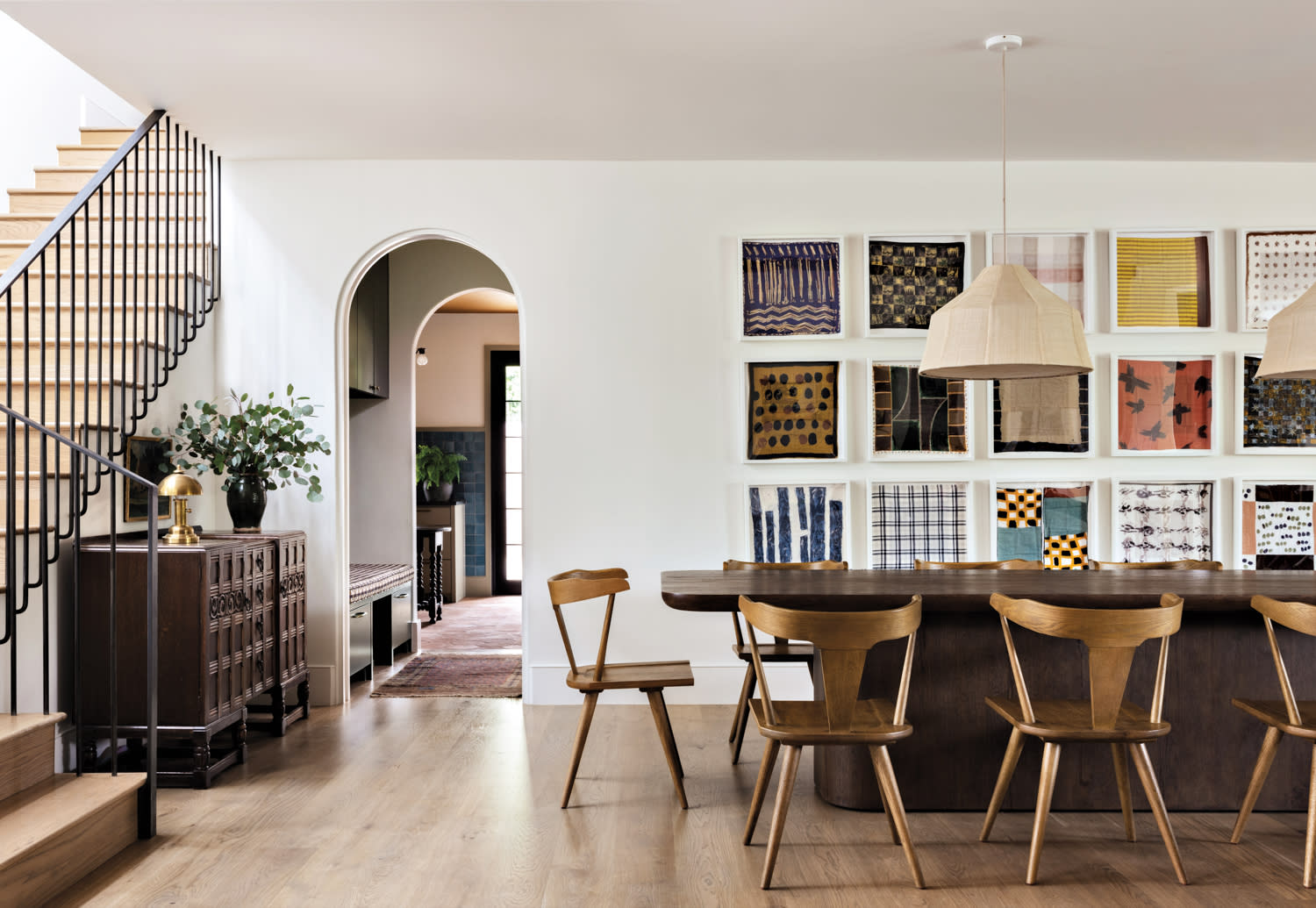 A wood dining table and chairs sit in front of a collection of framed vintage handkerchiefs.