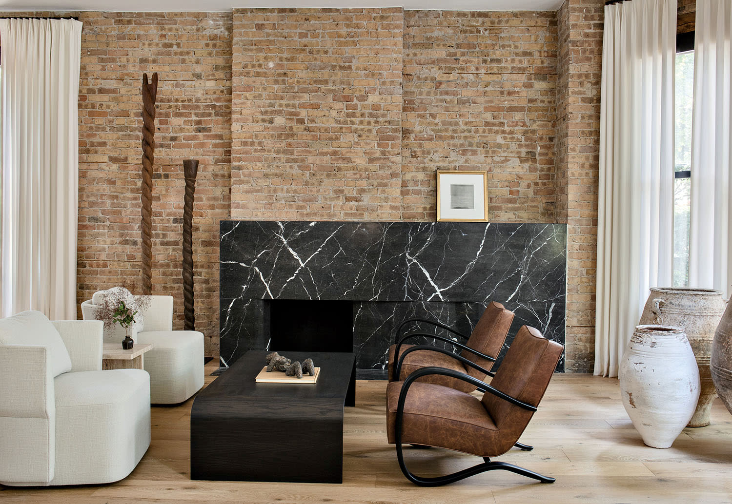 Two white fabric chairs face two brown leather chairs set near a stone fireplace and brick walls.