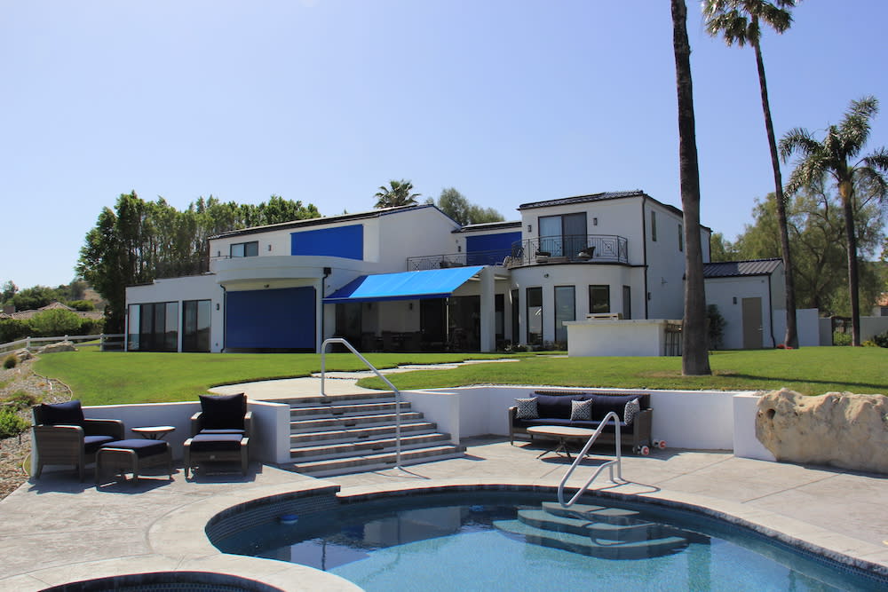 exterior of a modern white home with solar screens, retractable awnings and round pool