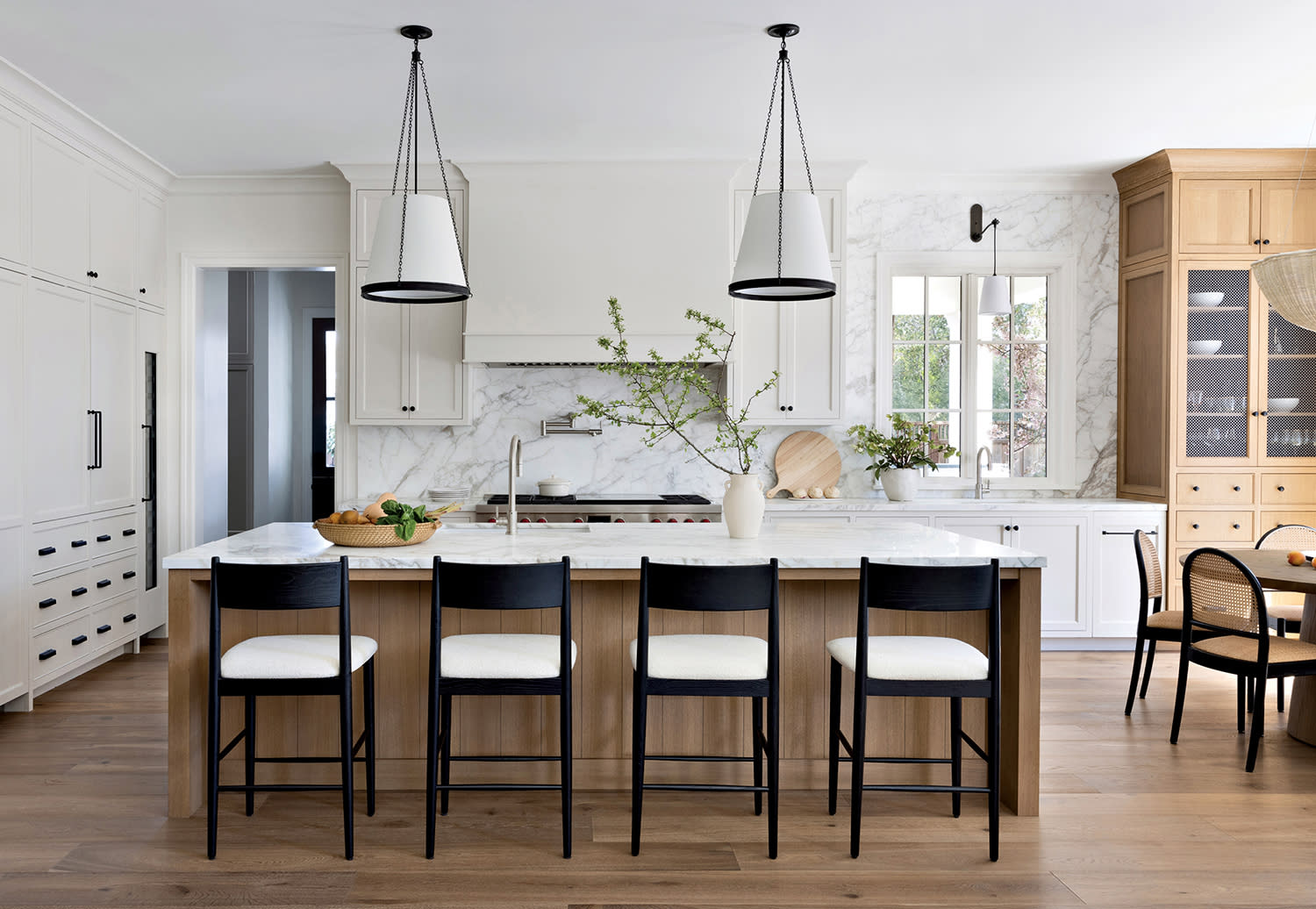 white kitchen with a marble backsplash and islands topped with Visual Comfort pendants