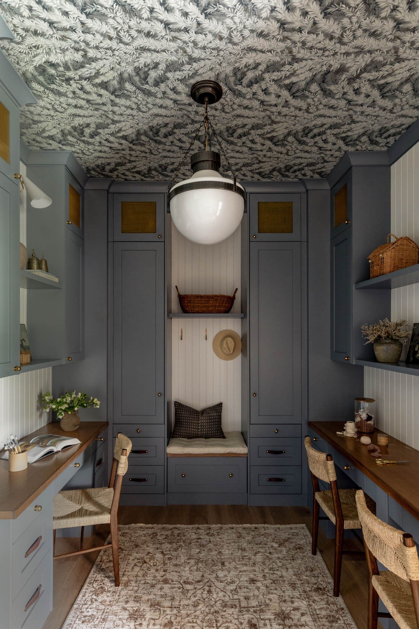 Cozy study nook with gray cabinets, wooden desks, and wicker chairs. Ornate ceiling pattern, central pendant light, and warm tones create a tranquil ambiance.