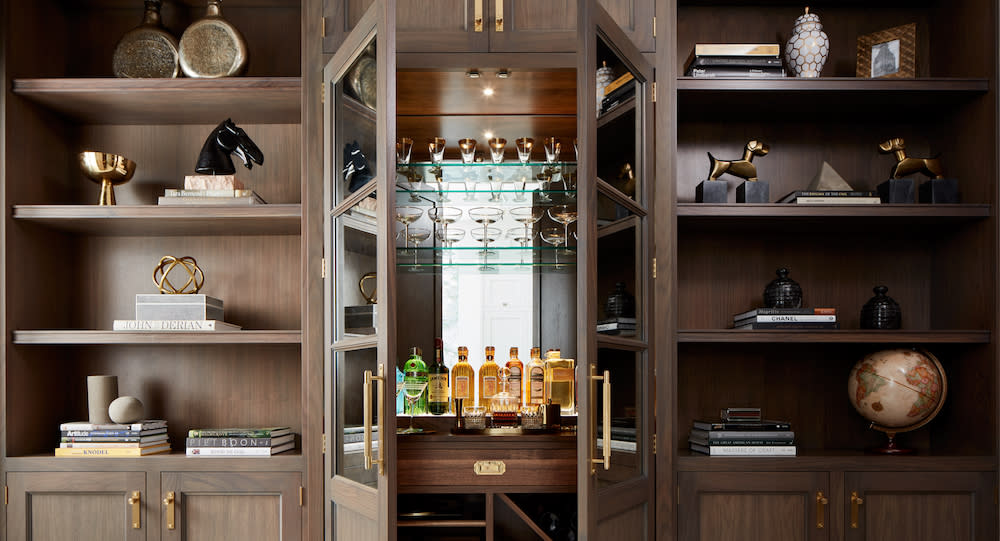 Walnut cabinetry with open shelving at the top and bar in the center with glass shelves and gold hardware.