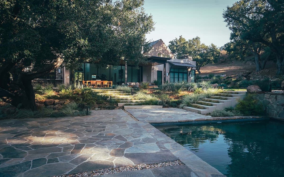 A stone walkway leads to a serene pool surrounded by lush trees, creating a tranquil outdoor setting
