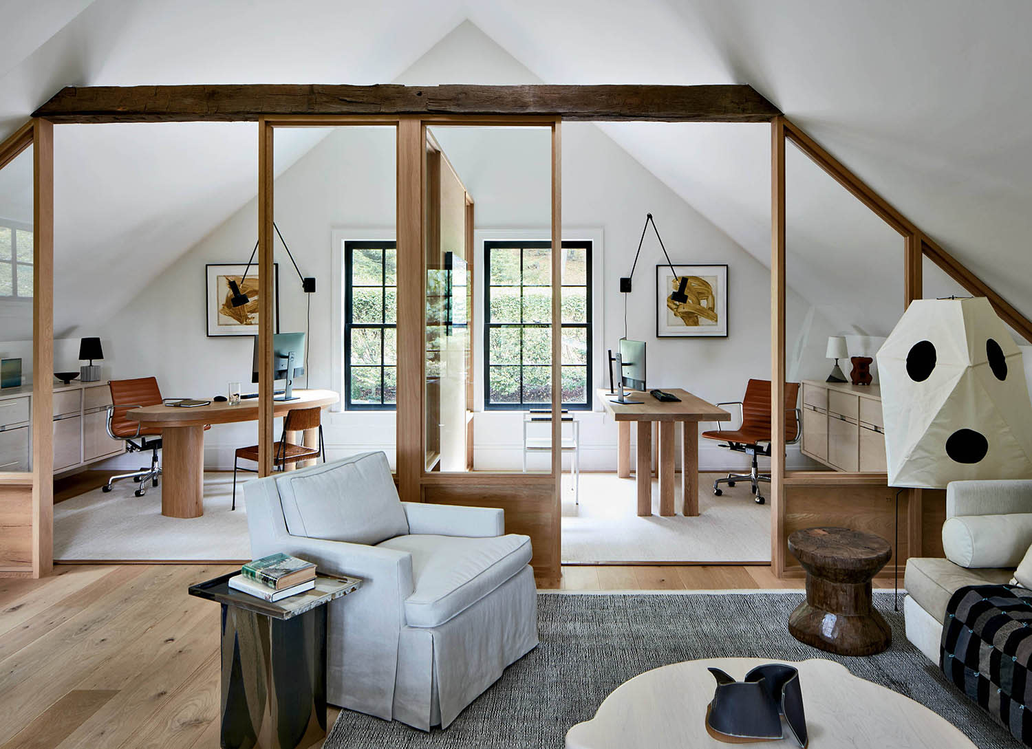 Two adjoining offices, each decorated with a desk, chairs and artwork, with a sitting area outside.