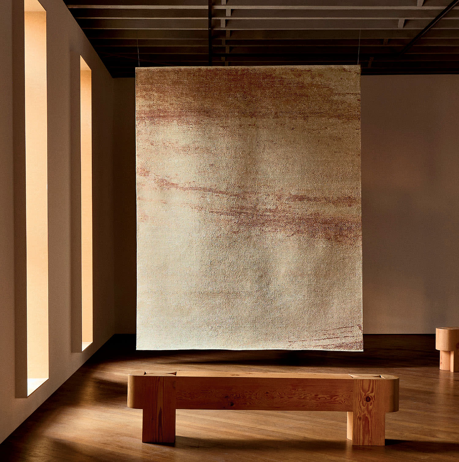 A tapestry with a rippling pattern hangs from the ceiling in a room with windows and a bench.