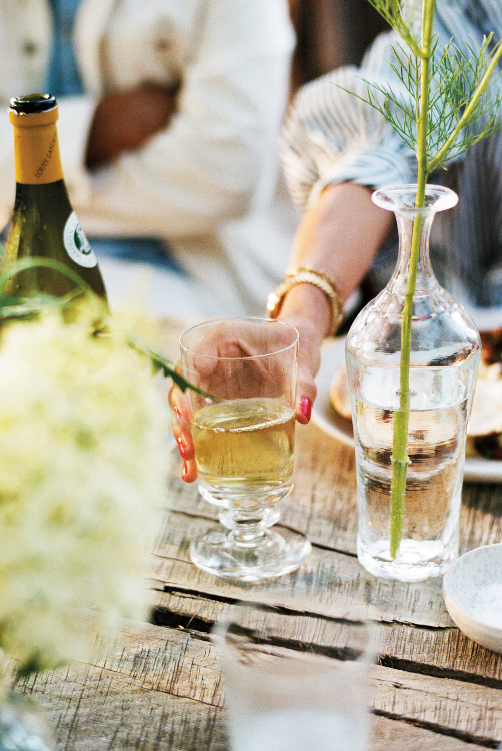 woman reaches for a glass at an outdoor dinner party