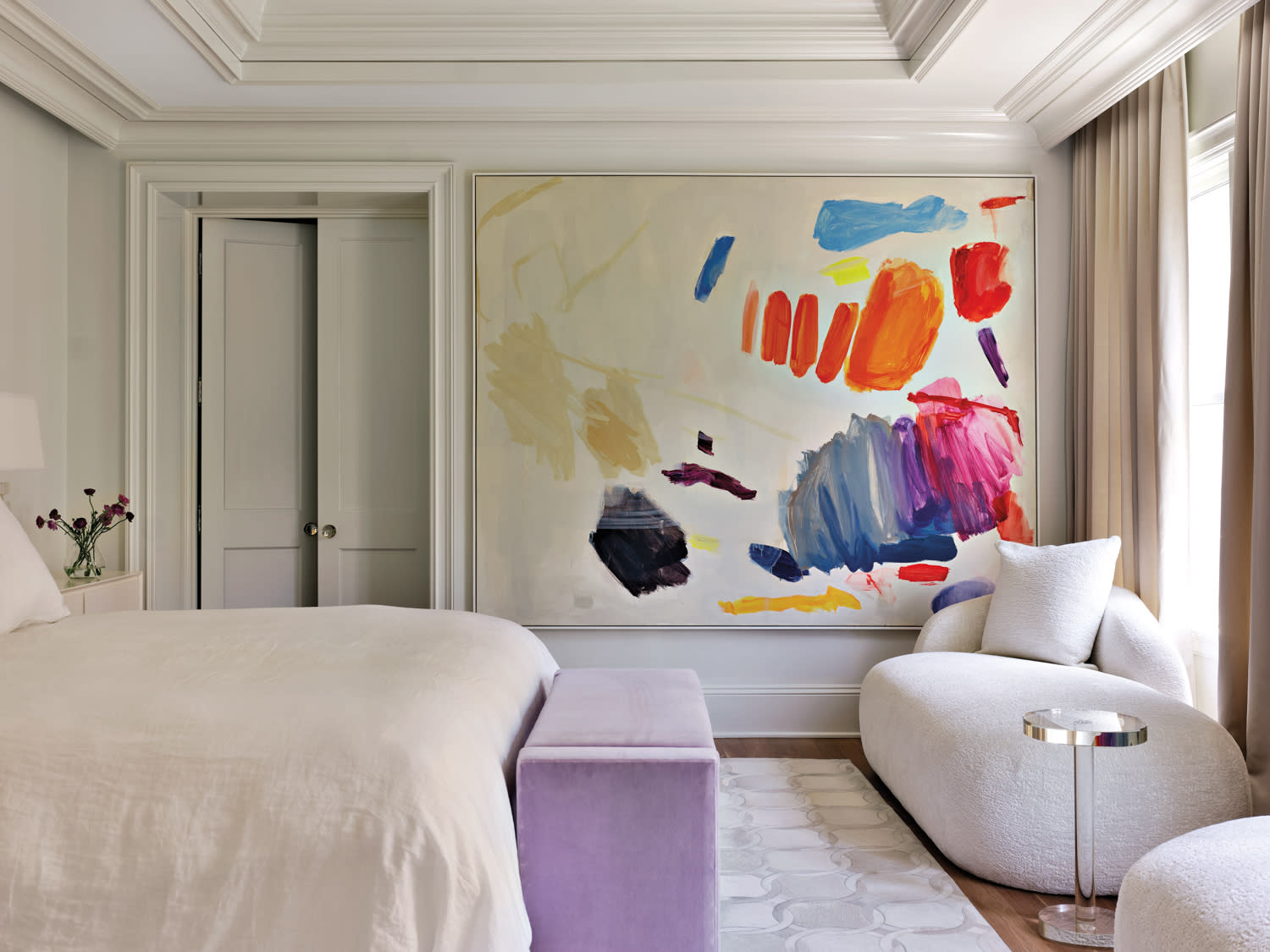 A modern bedroom with a large abstract painting featuring vibrant colors like red, blue, and orange. 