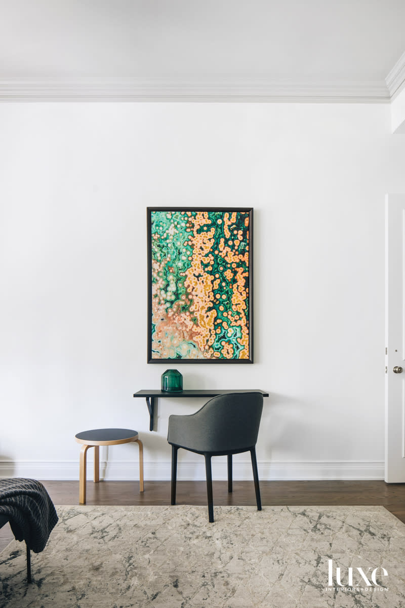 A green-and-orange contemporary artwork hangs above a black wall-mounted desk.