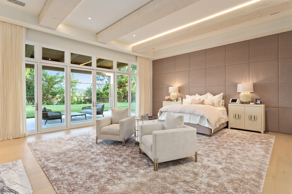 Modern spacious neutral bedroom featuring a large bed, sitting area and glass sliding door.