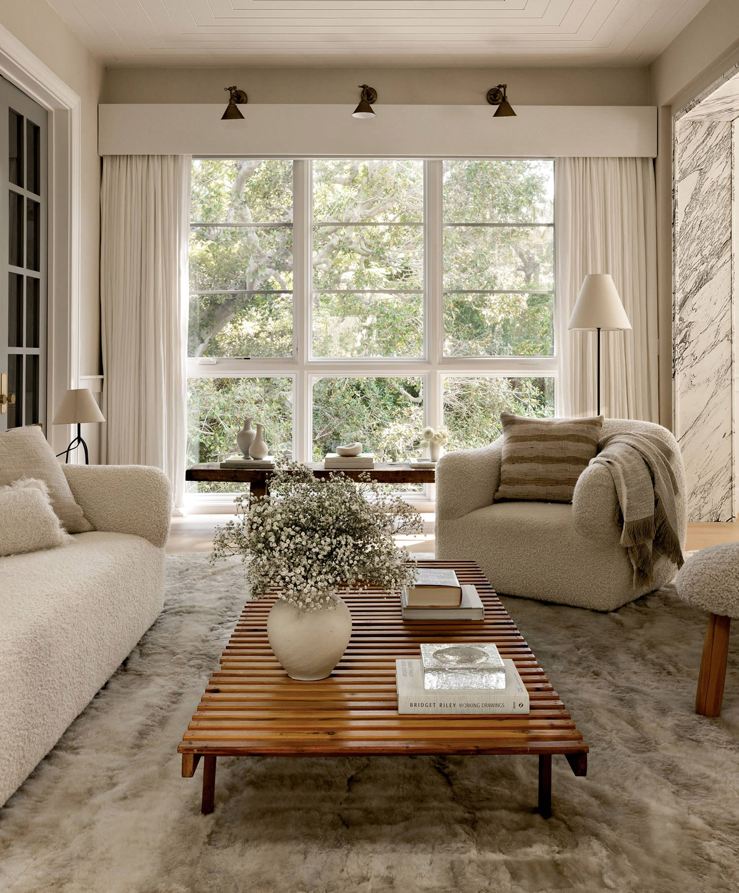 A pale couch and matching armchair set next to a wood-slat table decorated with a plant and books.