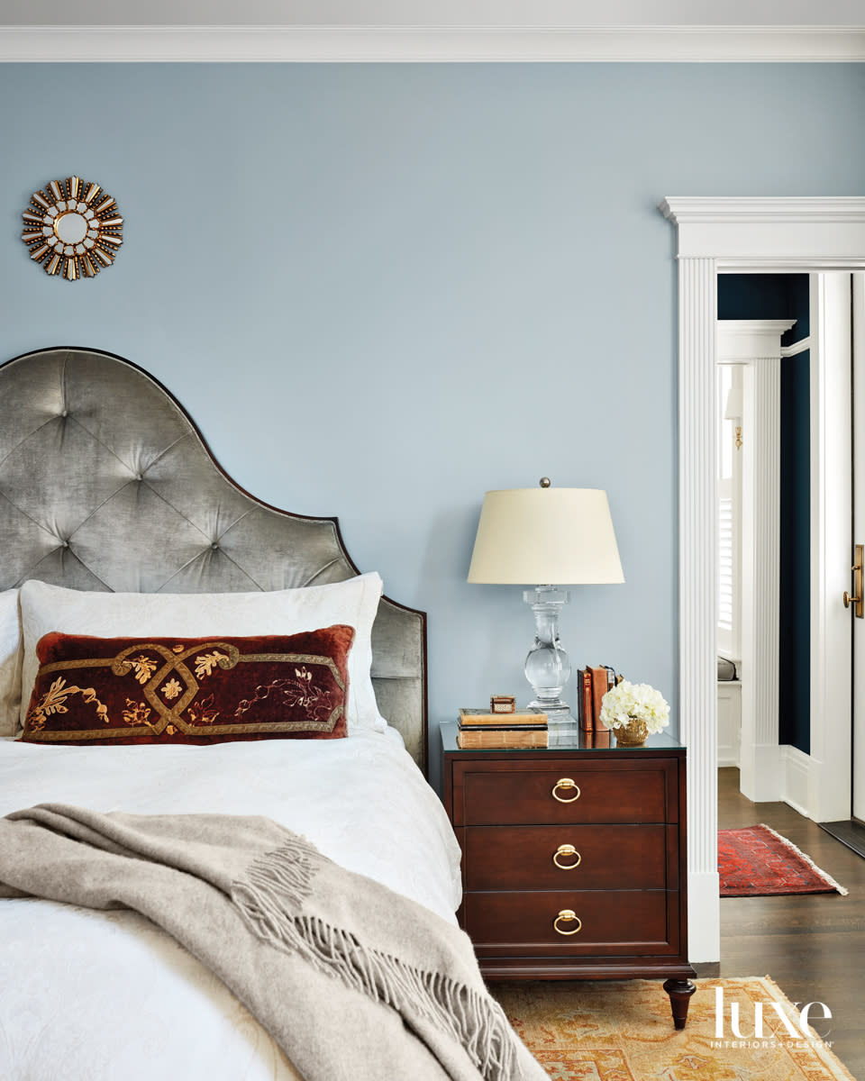 A blue bedroom with a gray velvet bed and gold rug.