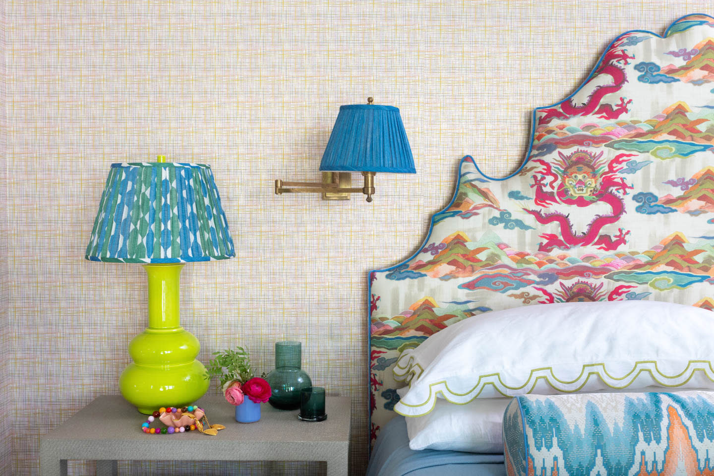 Eclectic bedroom with a colorful dragon-patterned headboard, blue and green lamps, and vibrant accessories on a gray nightstand, creating a lively atmosphere.